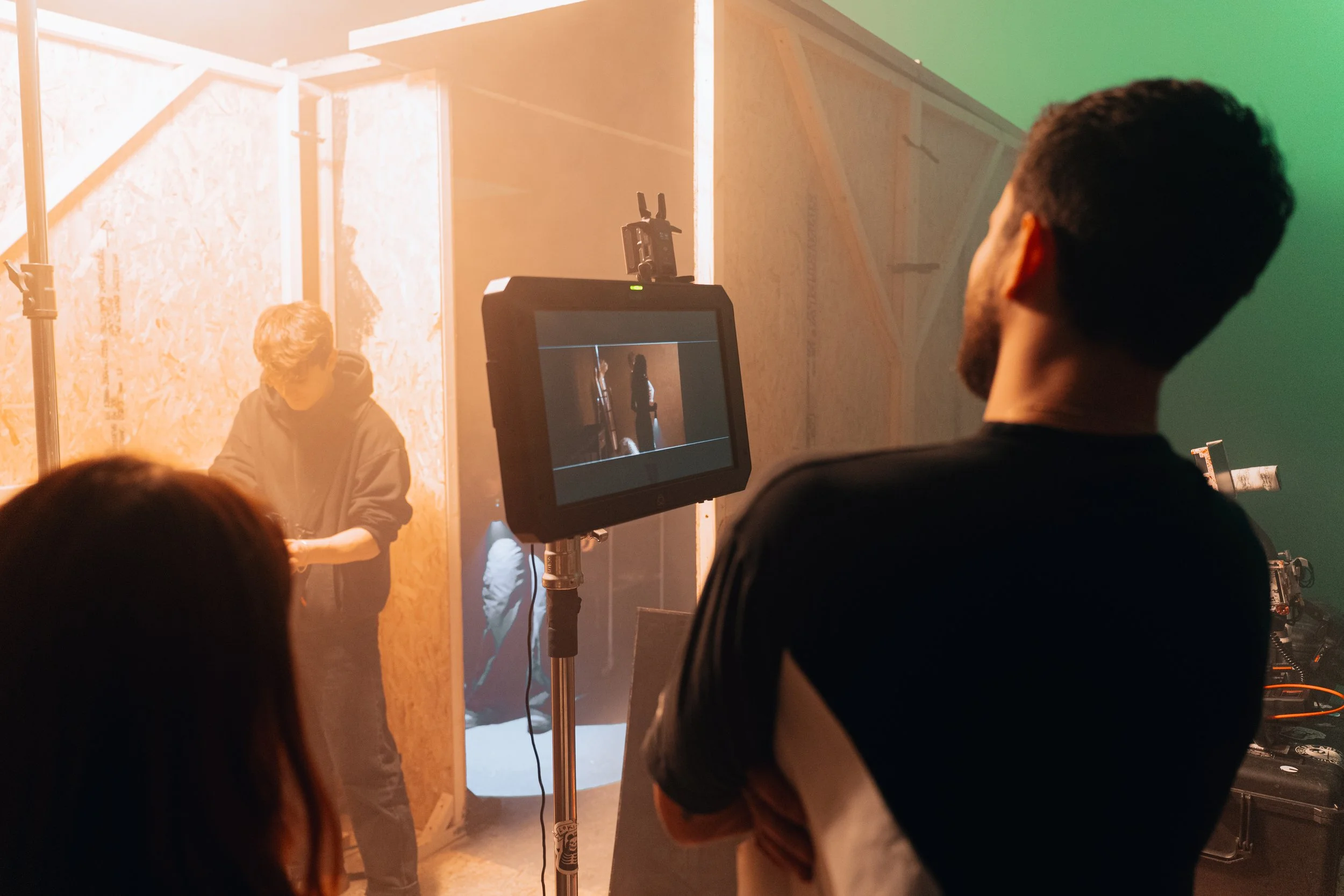 People filming a scene on a movie set with wooden walls and green and orange lighting.