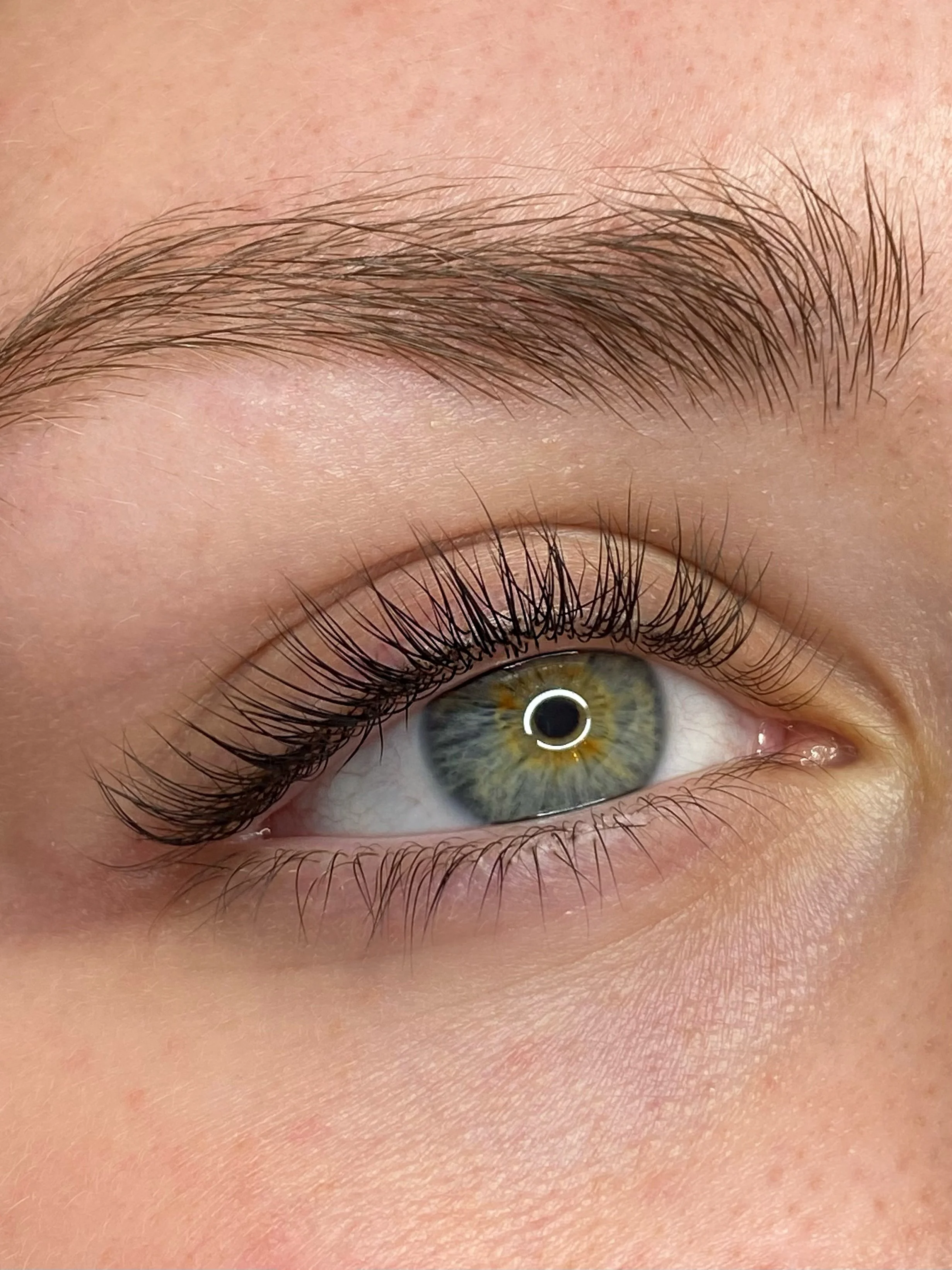 Close-up of a person's eye with green iris and long eyelashes, with a well-groomed eyebrow above.