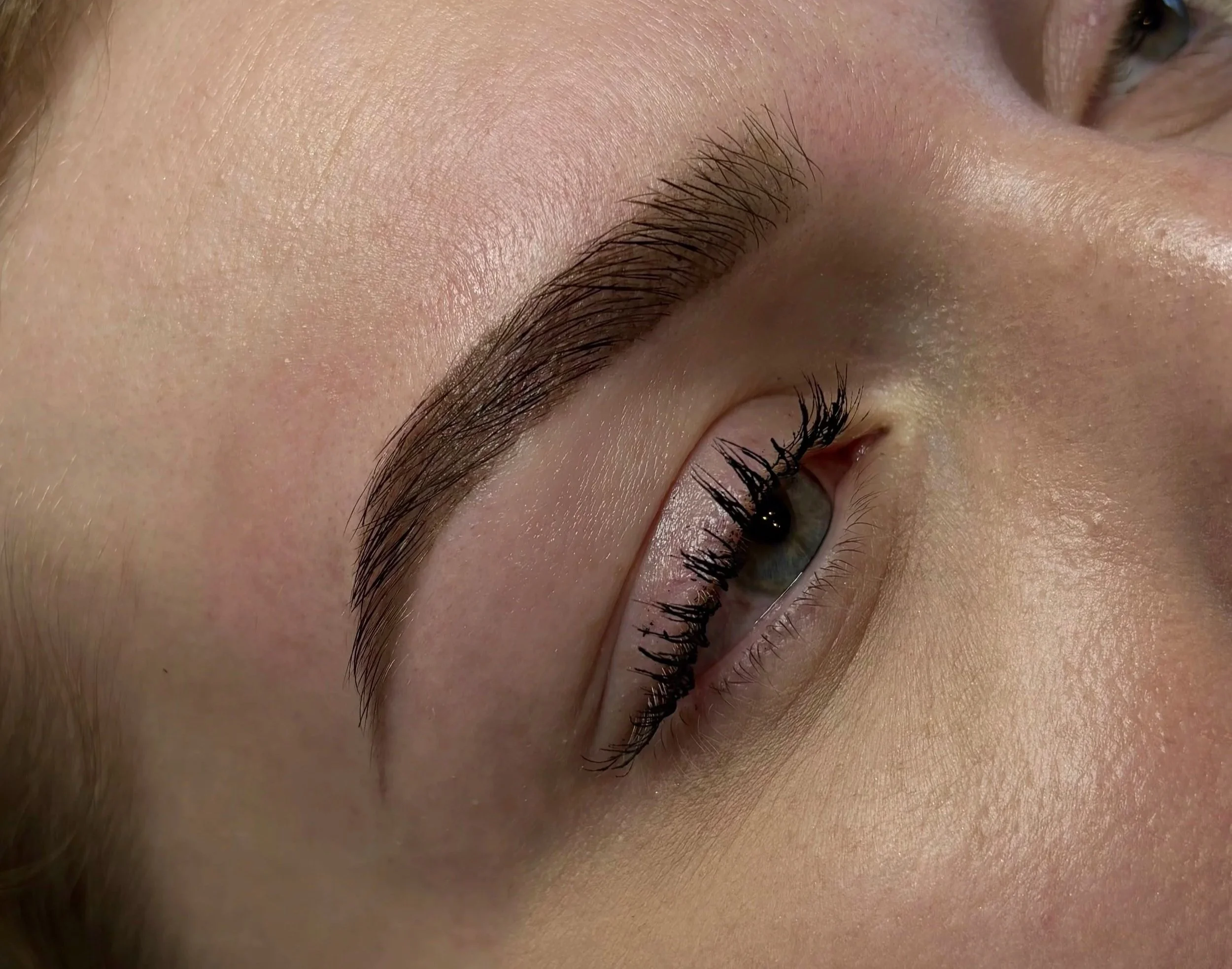Close-up of a woman's closed eye, showing well-groomed eyebrows, long dark eyelashes, and smooth skin.
