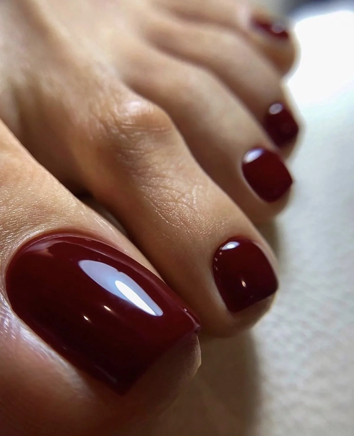 Close-up of a hand with dark red, glossy painted fingernails.