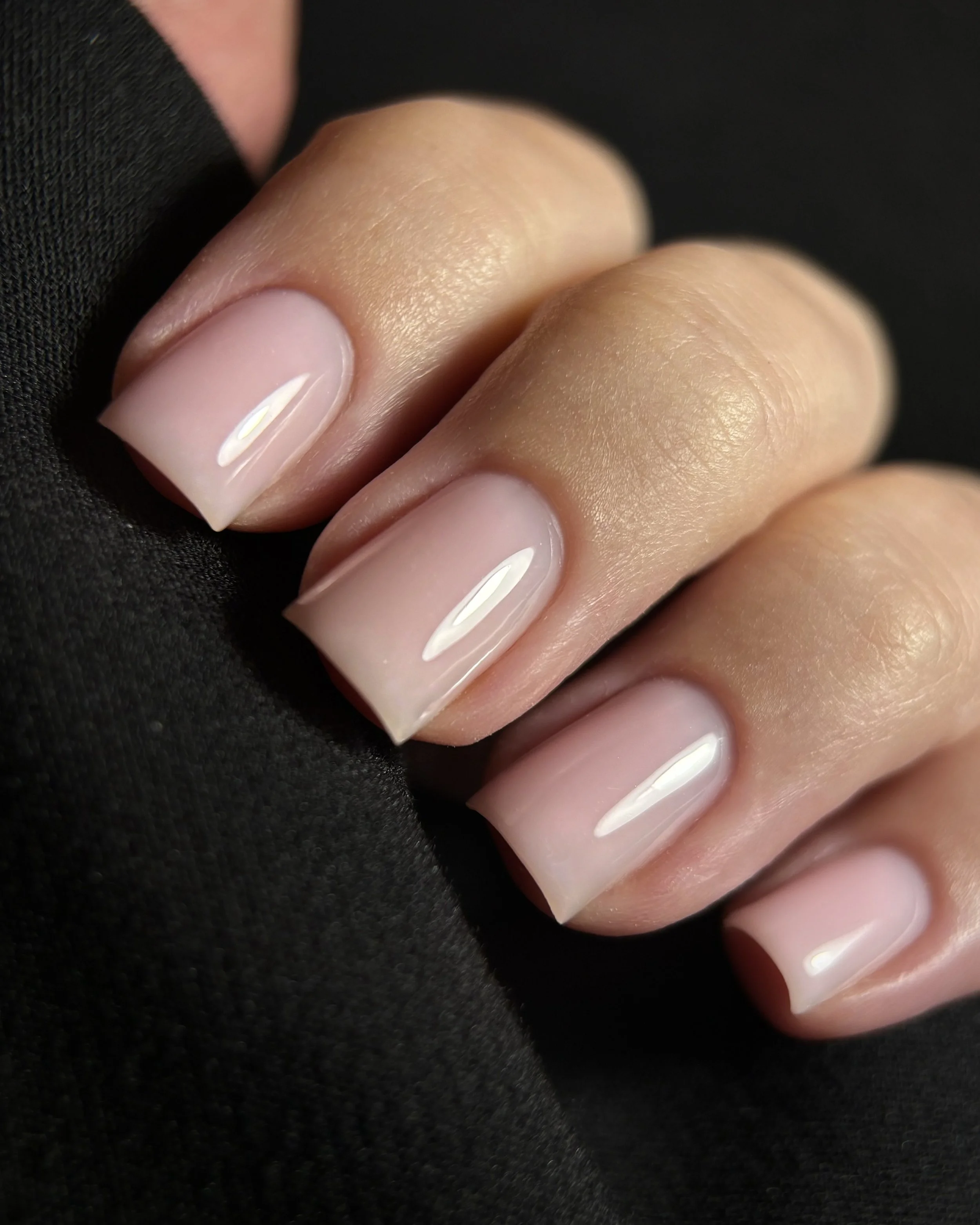 Close-up of a person's fingers with natural, polished nails resting on a black fabric surface.