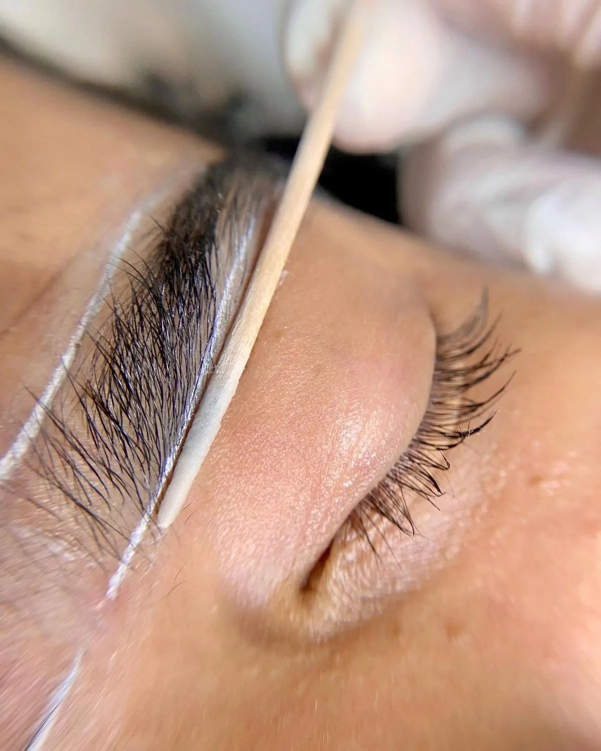 A close-up of a person's closed eye during an eyelash extension procedure with a tool applied along the lash line.