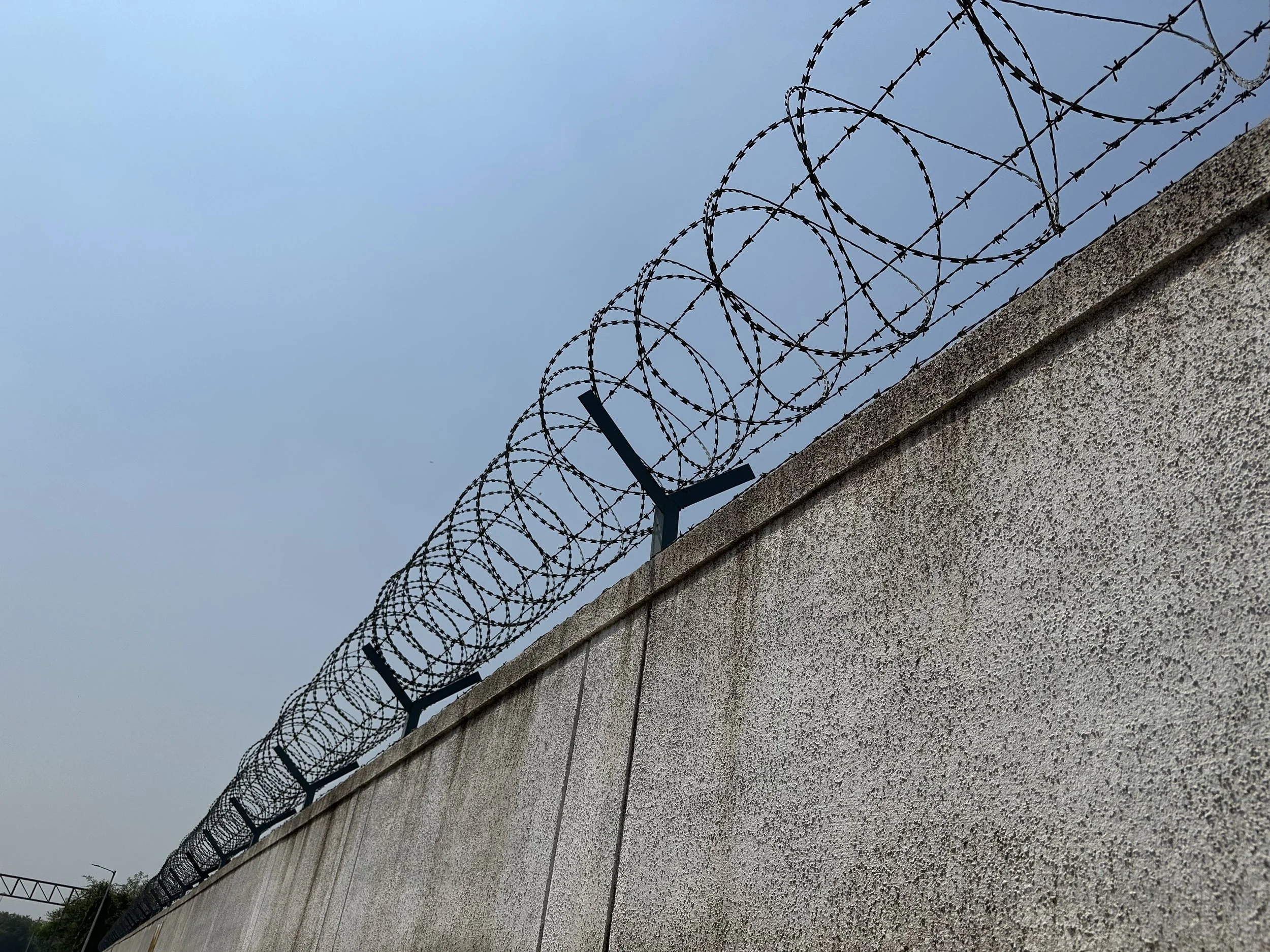 Barbed wire coiled on top of a concrete wall under a cloudy sky.