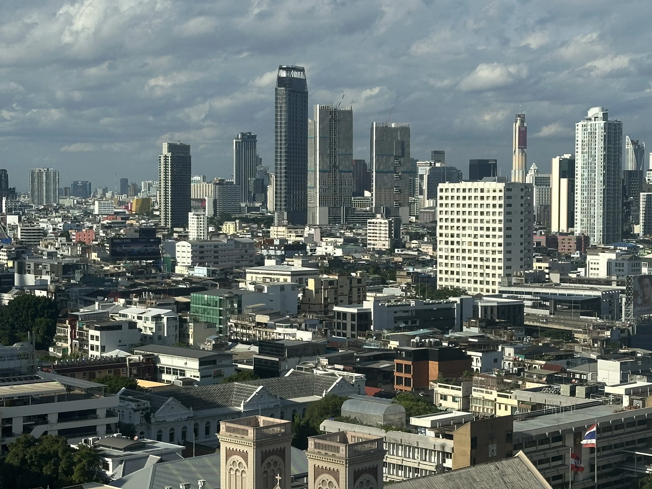 City skyline with tall skyscrapers under a partly cloudy sky, featuring modern and historic buildings.
