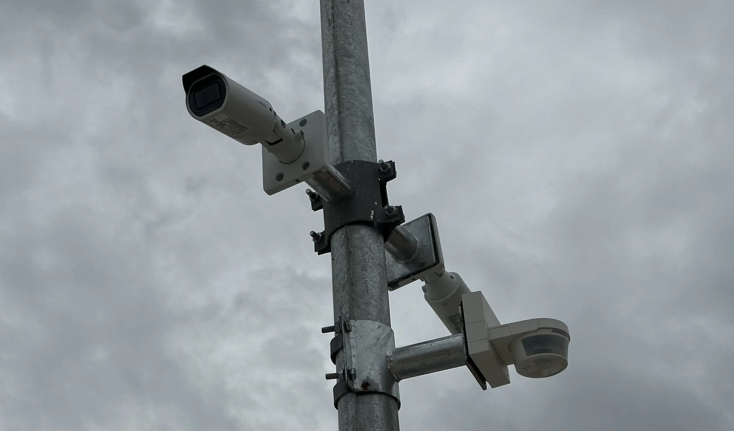 Security cameras mounted on a gray metal pole against an overcast sky.