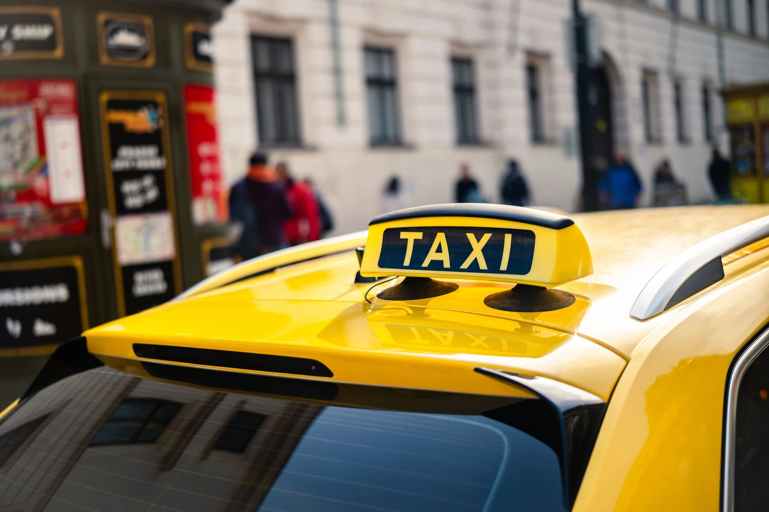 Close-up of a yellow taxi sign on the roof of a yellow taxi in an urban area.