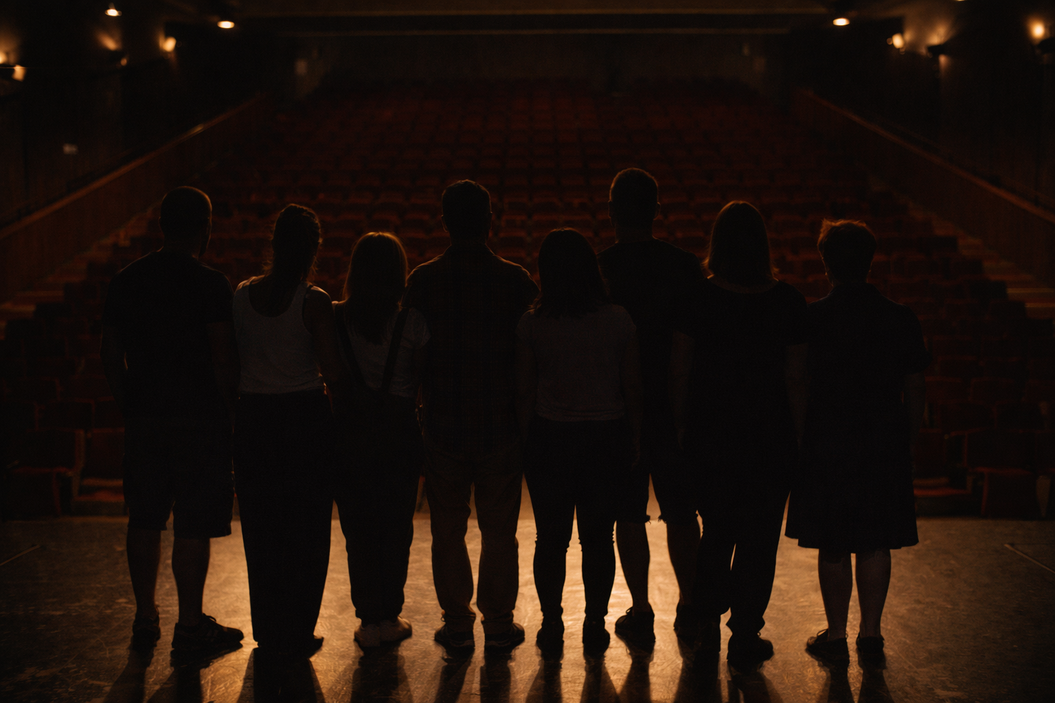 Grupo de personas de espaldas en un teatro oscuro, con filas de asientos vacíos al fondo.