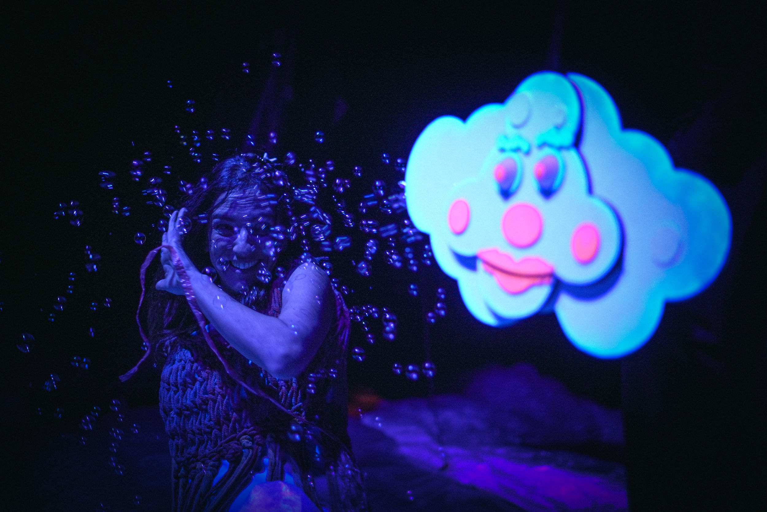 Persona sonriendo bajo agua en una exhibición con una figura de nube con rostro caricaturesco brillante en neón