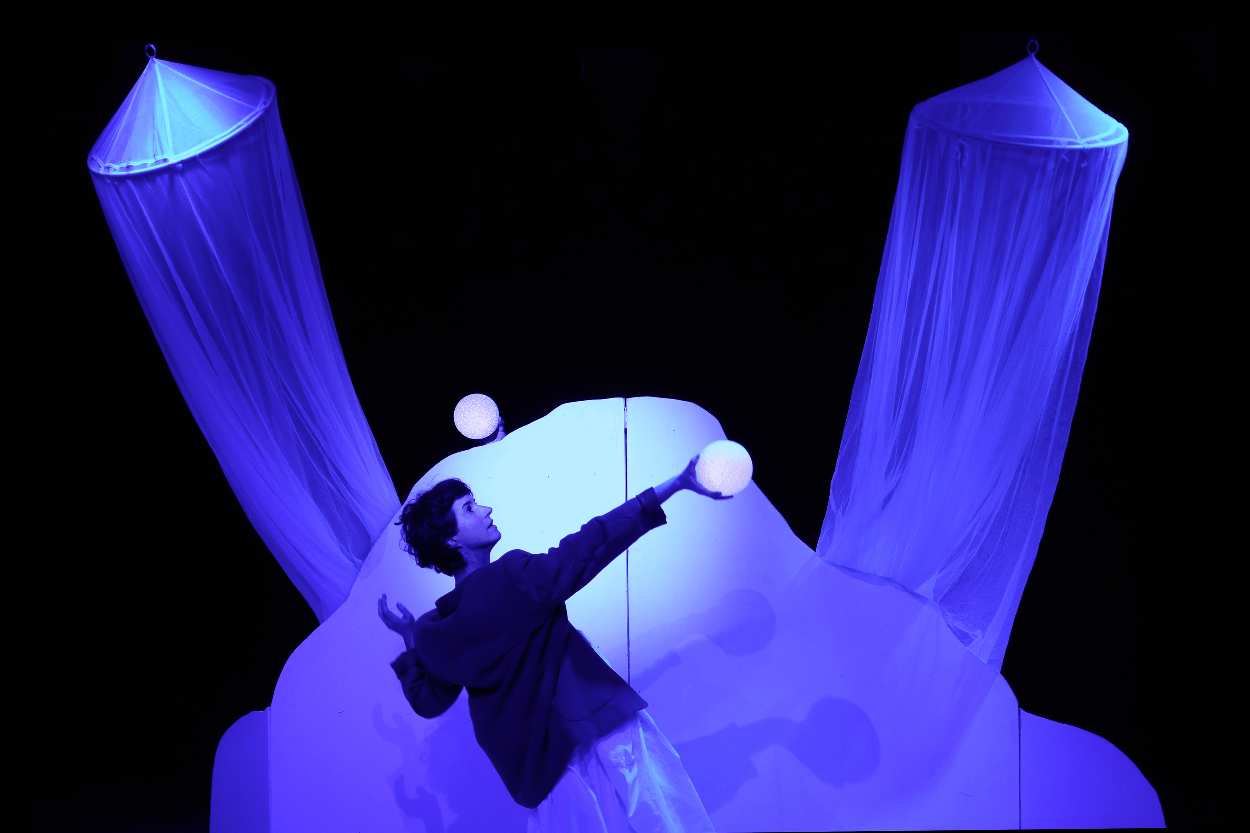 Joven actuando en escenario con estructura azul y luces blancas y azules, con telones de tela azul en el fondo.