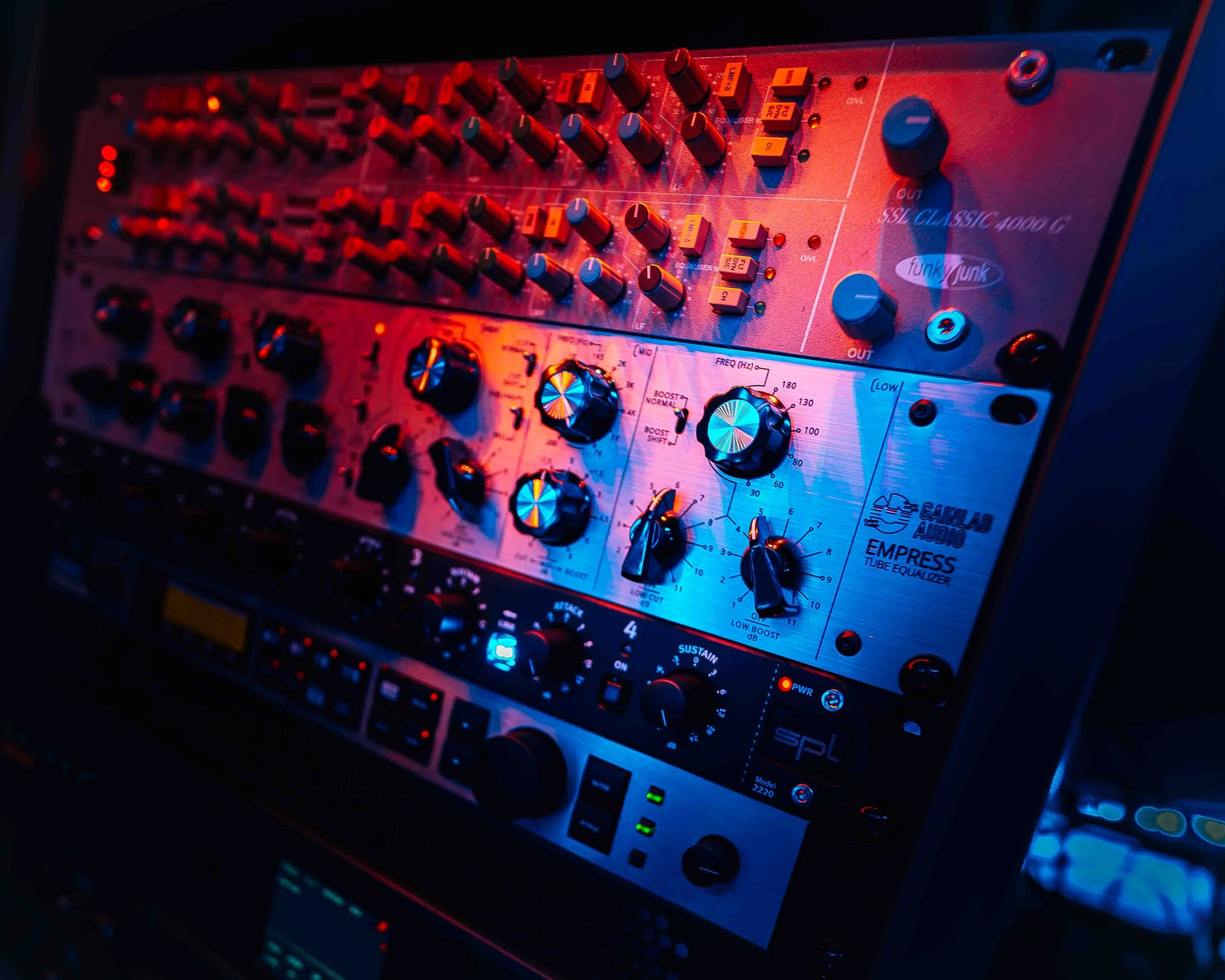 Close-up photo of a vintage synthesizer with various knobs, switches, and a small OLED screen, illuminated by red and blue lighting.