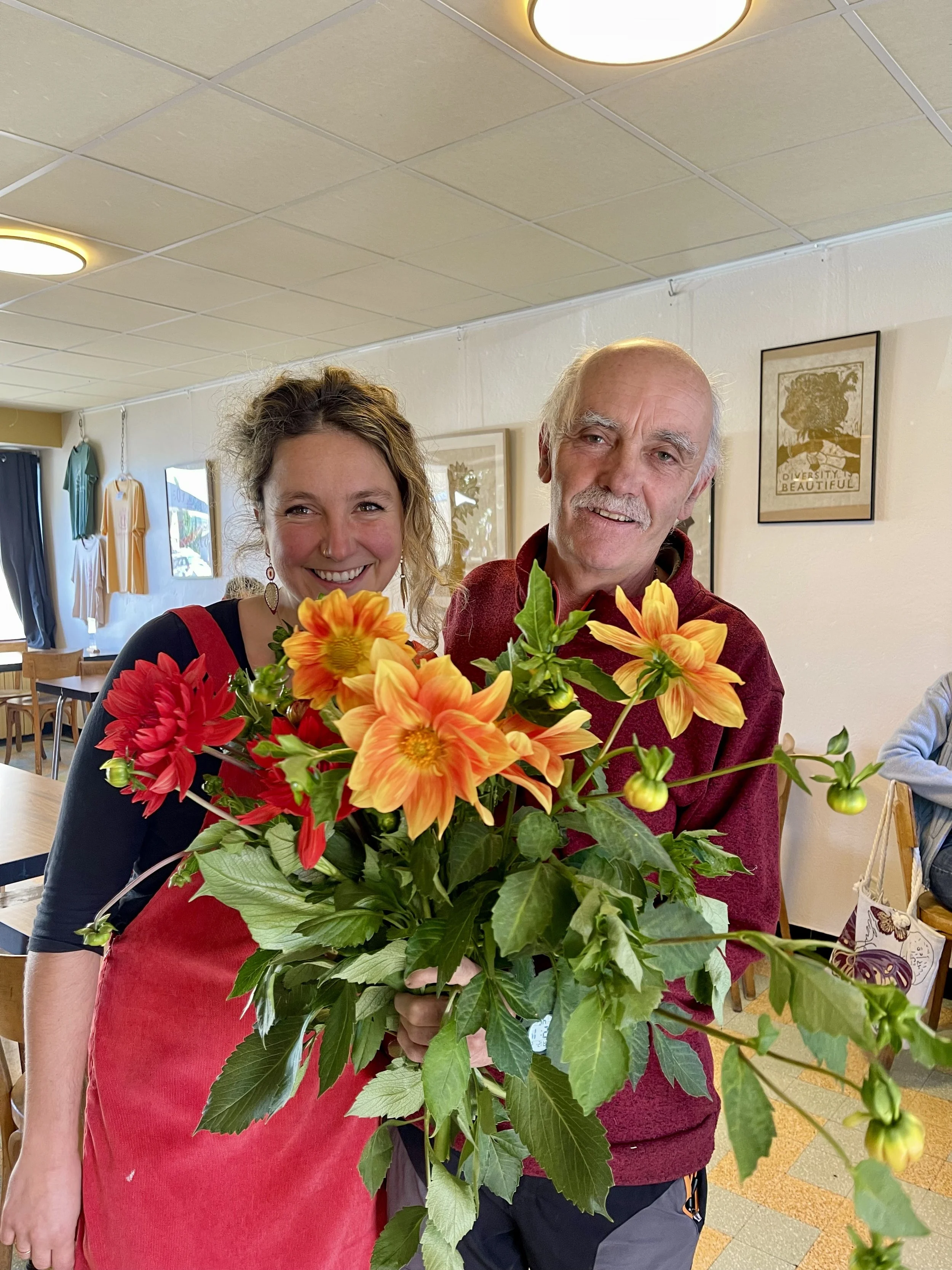 Deux personnes souriantes tiennent un bouquet de fleurs colorées dans un intérieur lumineux.