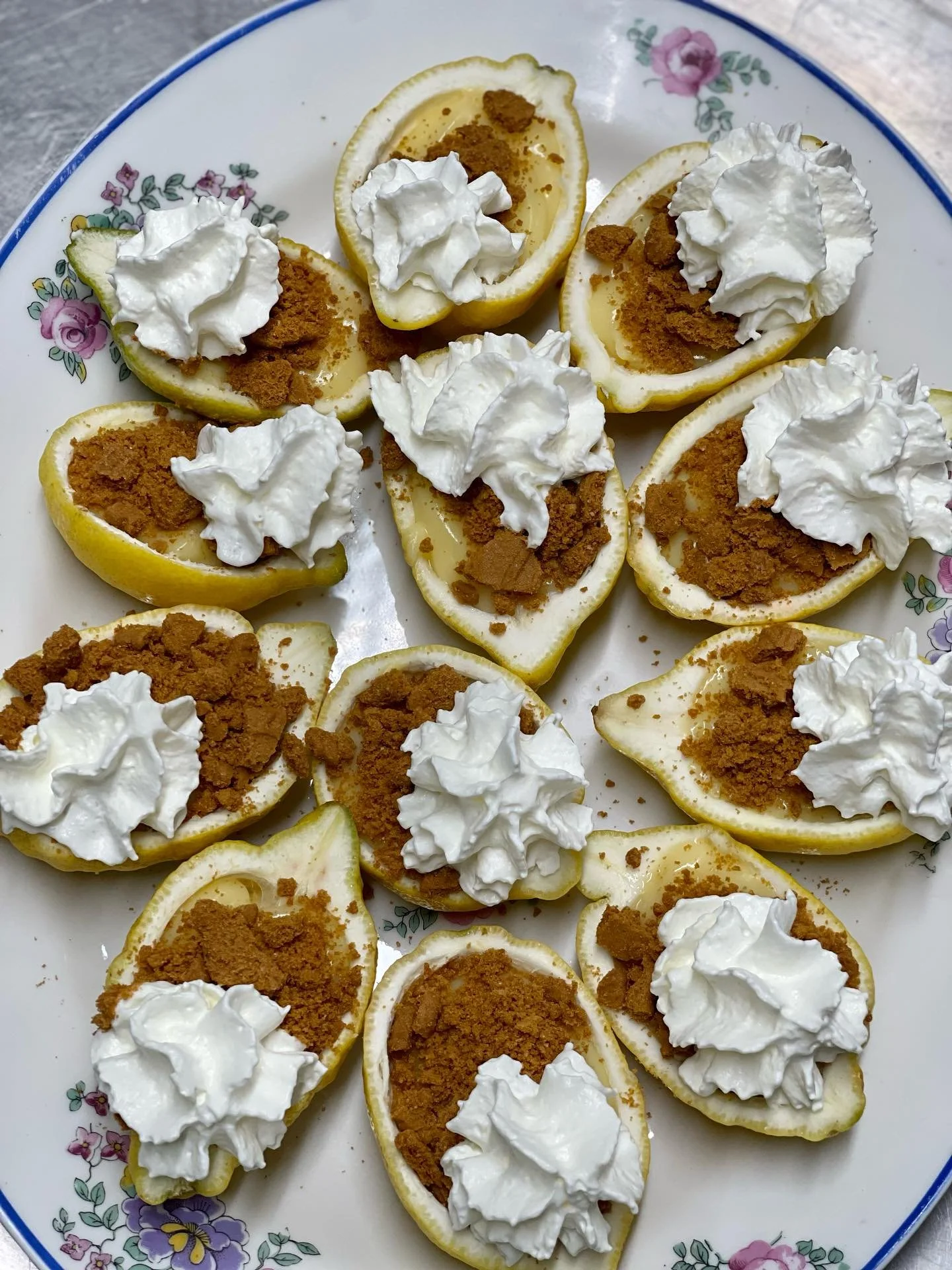 Plusieurs demi citrons garnis de crème, de biscuit émietté et de crème fouettée, servis sur une assiette en porcelaine à fleurs.