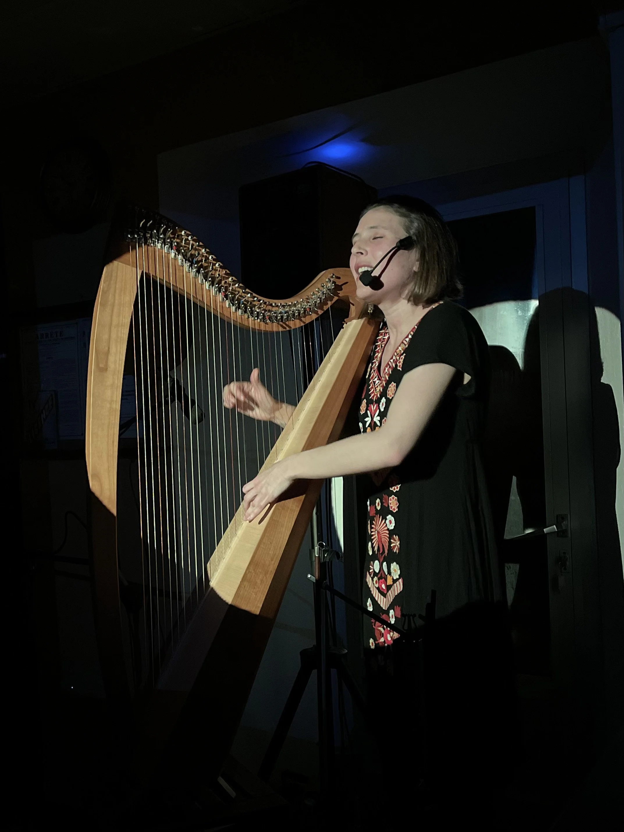 Femme jouant de la harpe lors d'une performance, portant un micro-cravate et se concentrant sur la musique.