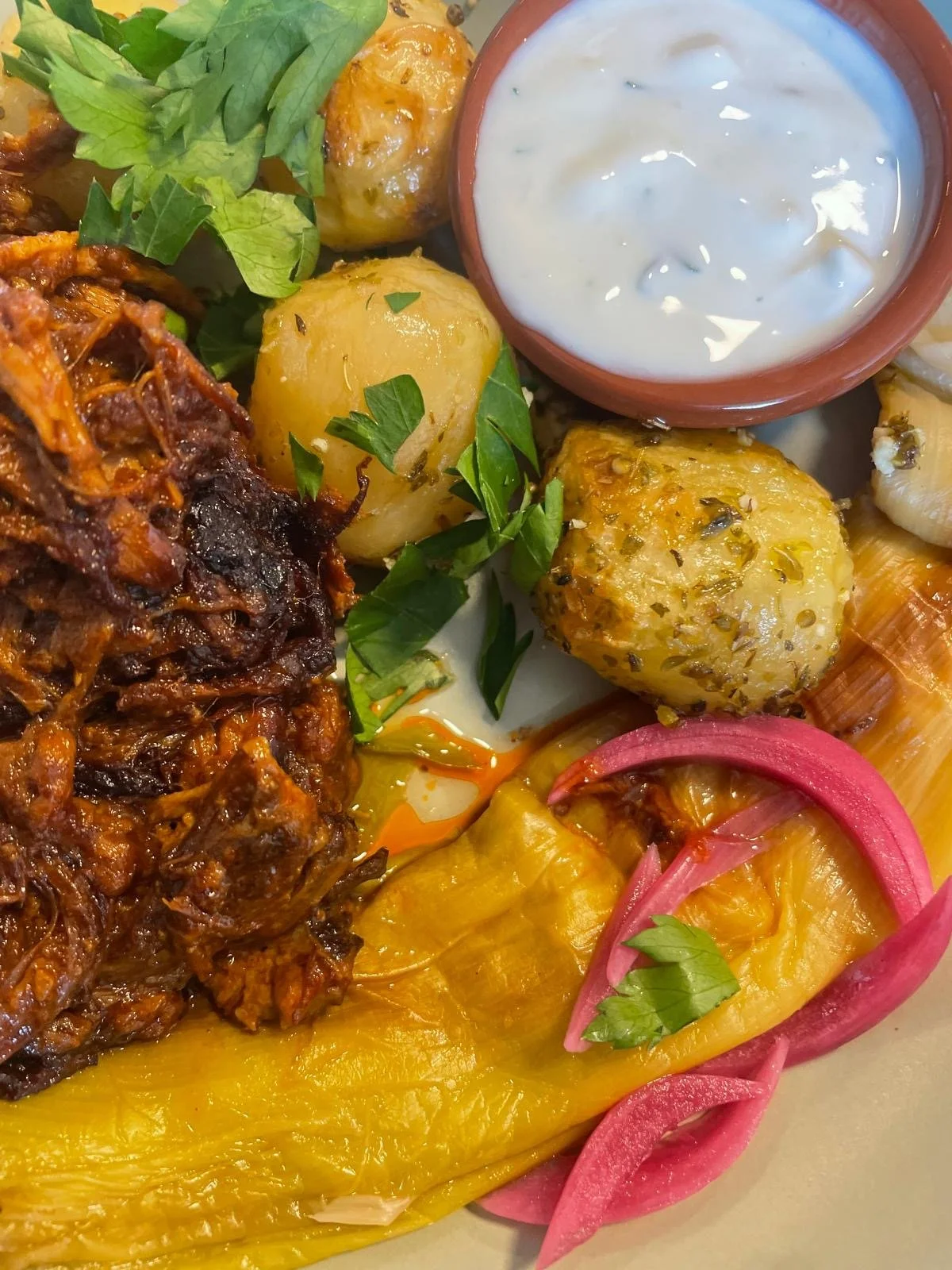Assiette de plats marocains avec pâtes, légumes, sauce blanche, viande braisée, oignons rouges et herbes.