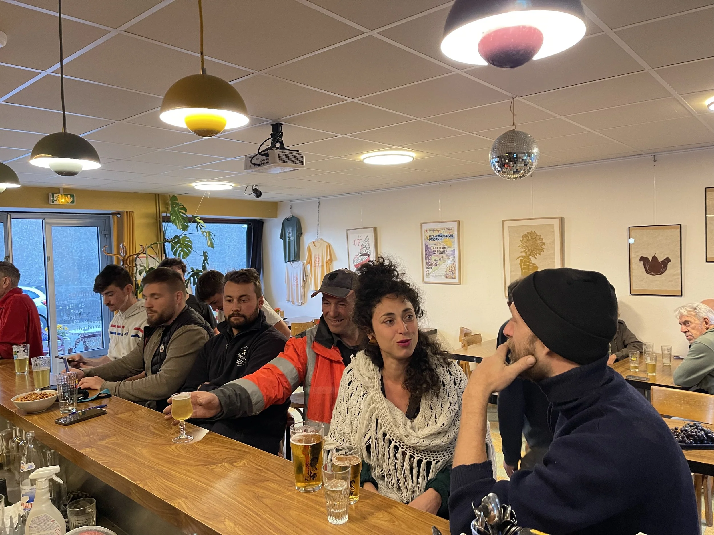Groupe de personnes discutant dans un bar ou un café, avec des boissons devant eux, pendant une soirée ou un rassemblement social.