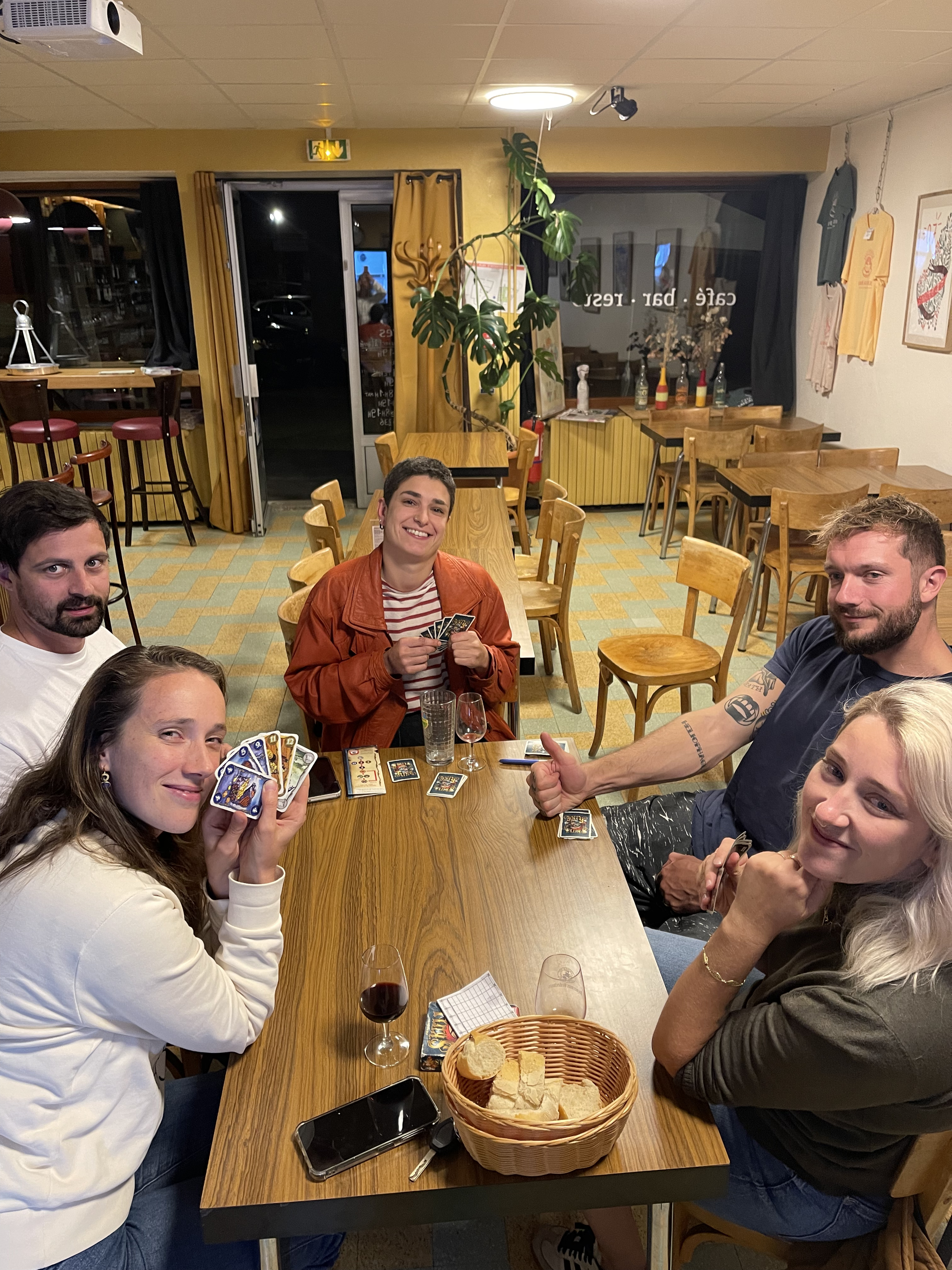 Cinq amis jouent aux cartes autour d'une table dans un café ou un restaurant.