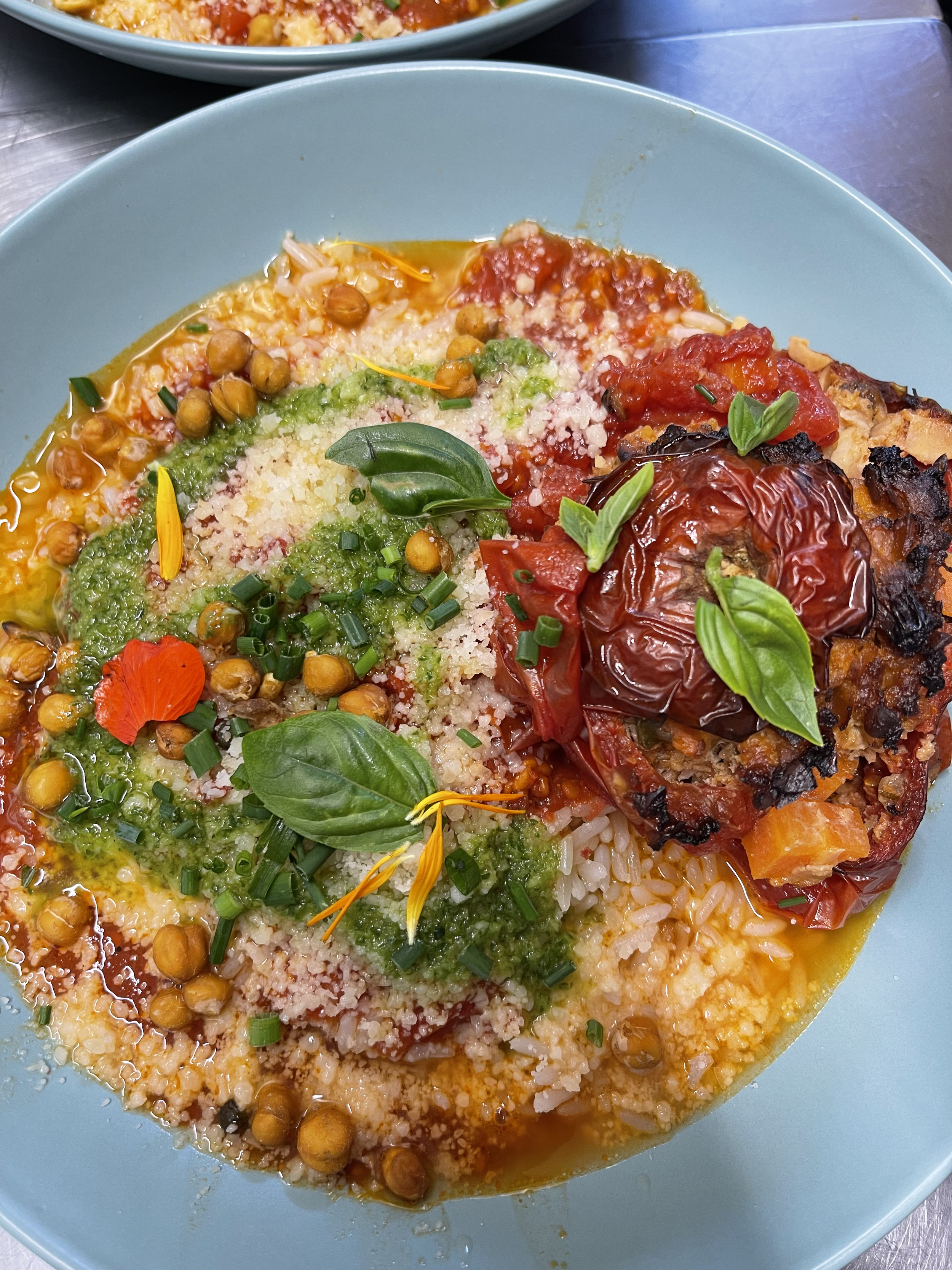 Plat de nourriture méditerranéenne avec du riz, des tomates, des féves, des herbes fraîches, des tomates rôties et du fromage parmesan râpé, présenté dans un bol bleu.