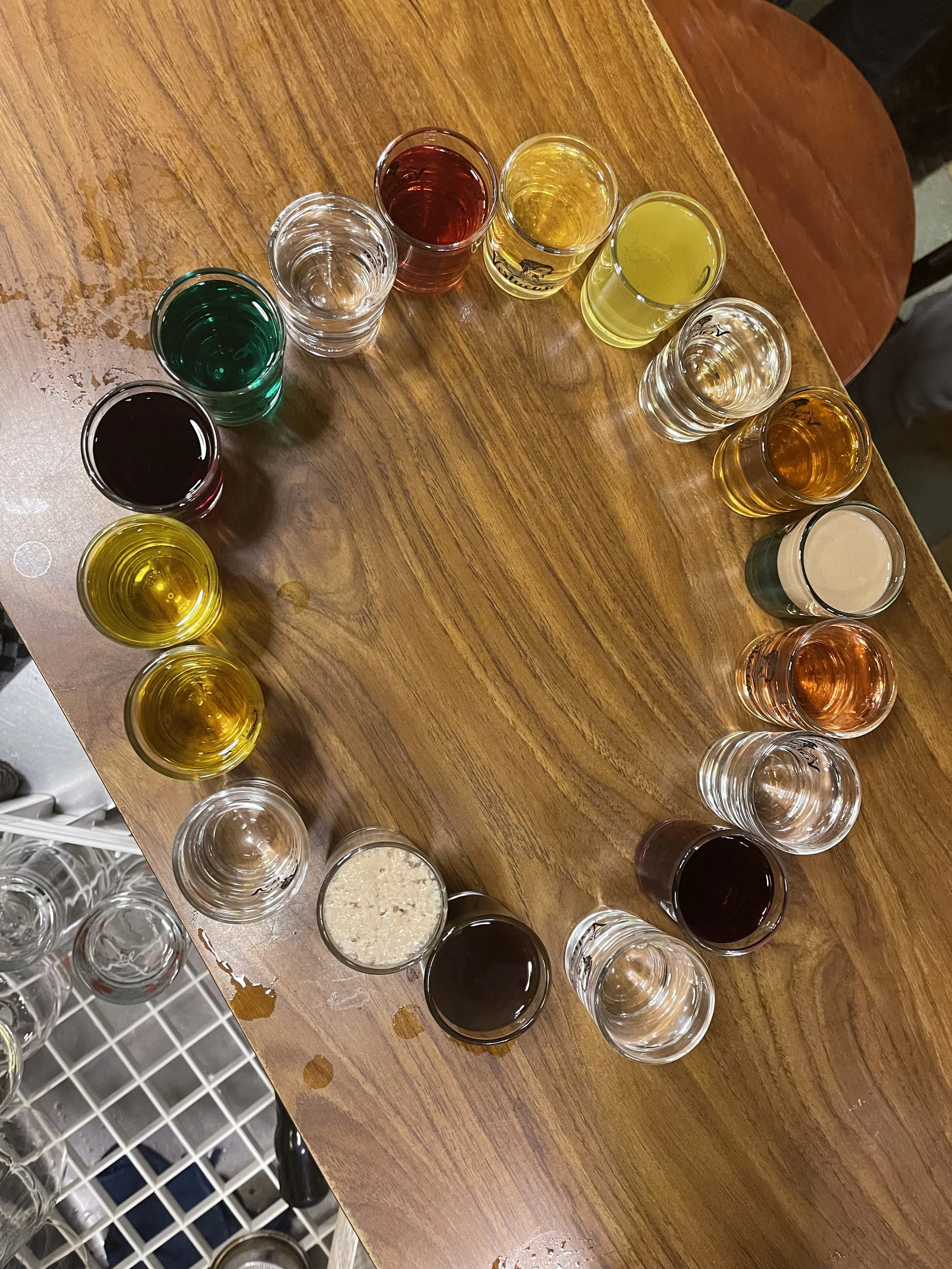 Verre de dégustation rempli de différentes boissons colorées disposés en cercle sur une table en bois.