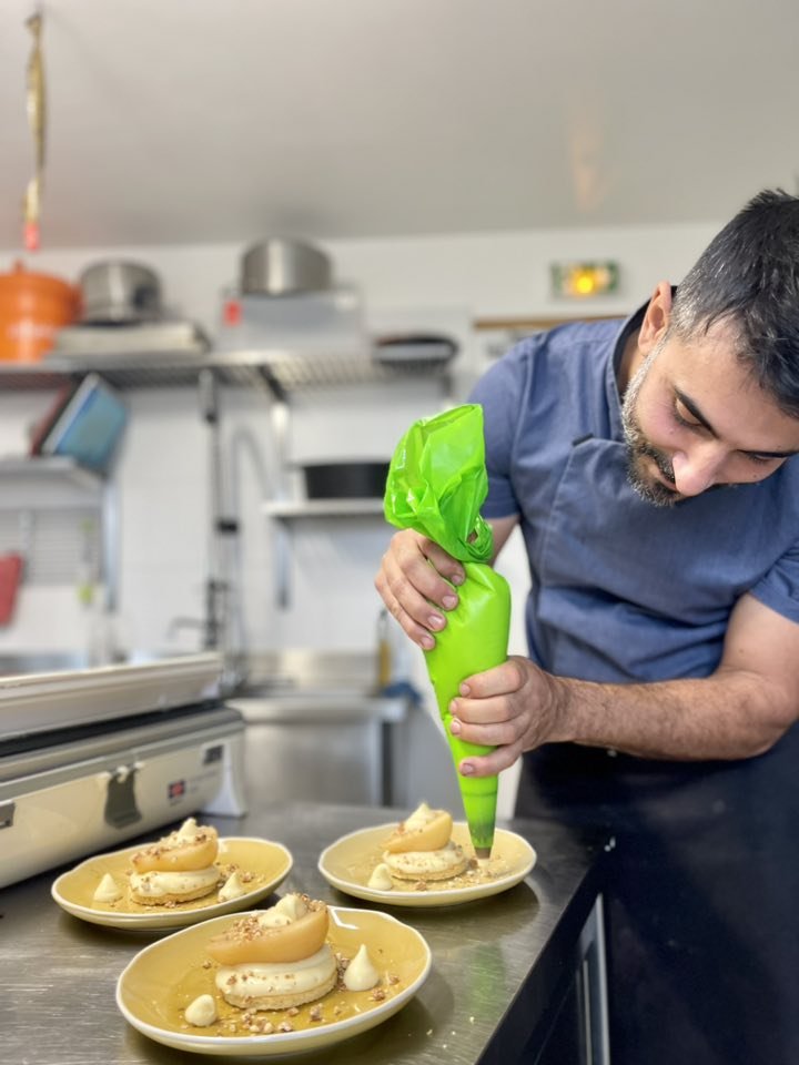 Chef décorant des desserts à l'aide d'une poche à douille verte dans une cuisine.