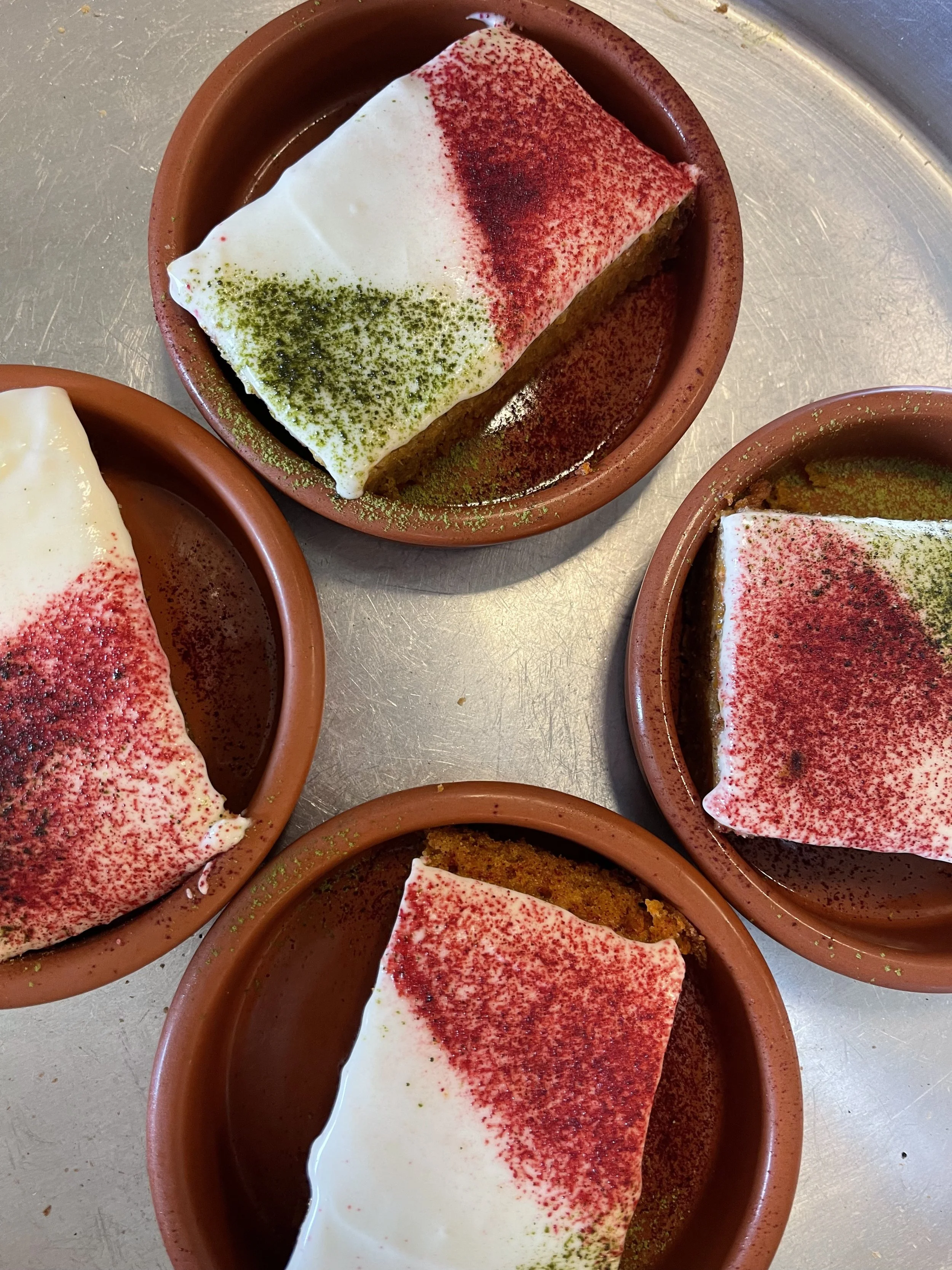 Quatre petits ramequins contenant un dessert à base de crème fouettée, de poudre de cacao, et de poudre de matcha, avec une portion de gâteau en dessous.