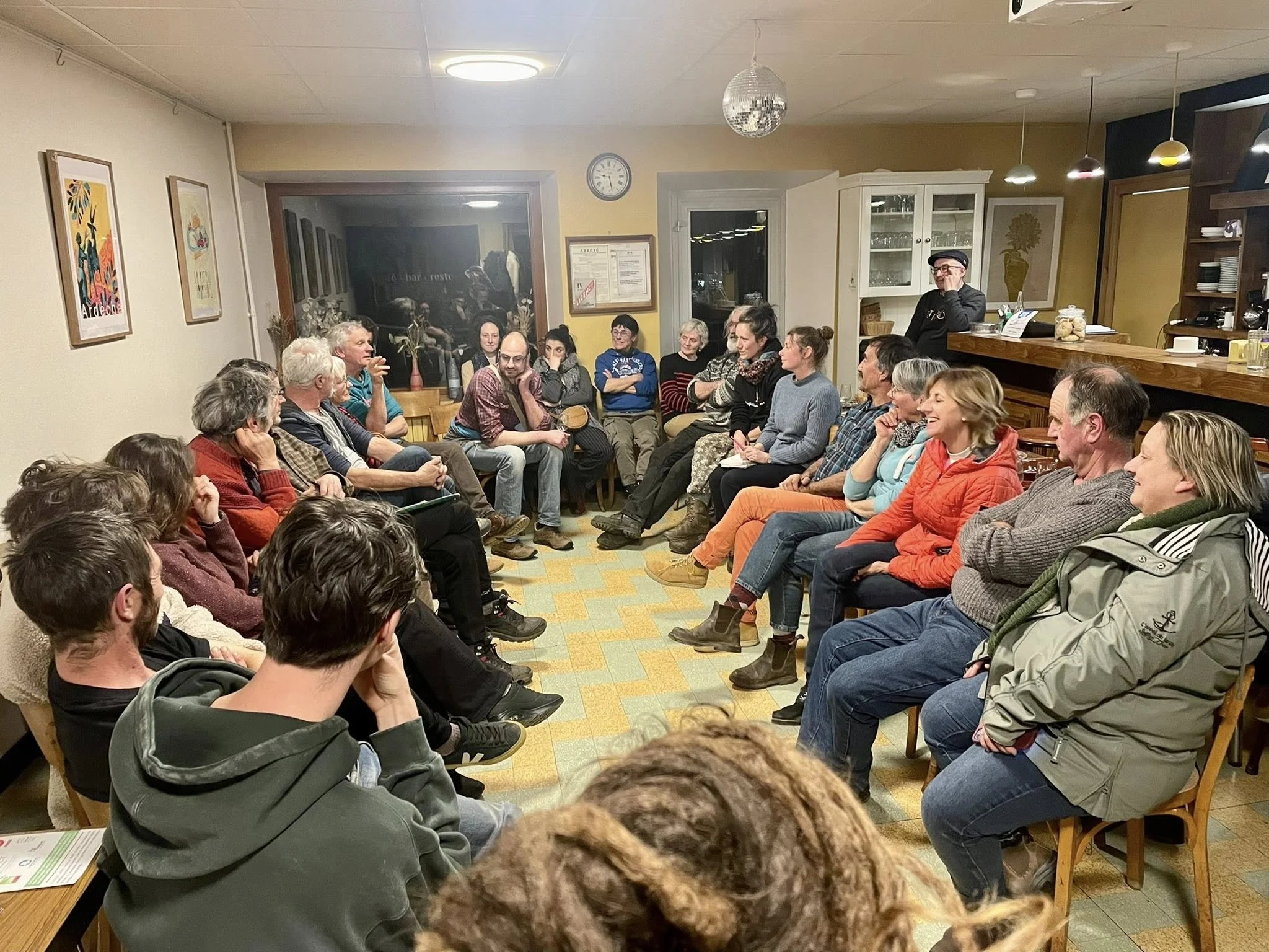 Groupe de personnes assises en cercle dans une pièce, discutant lors d'une réunion ou d'un atelier, avec un bar en arrière-plan.