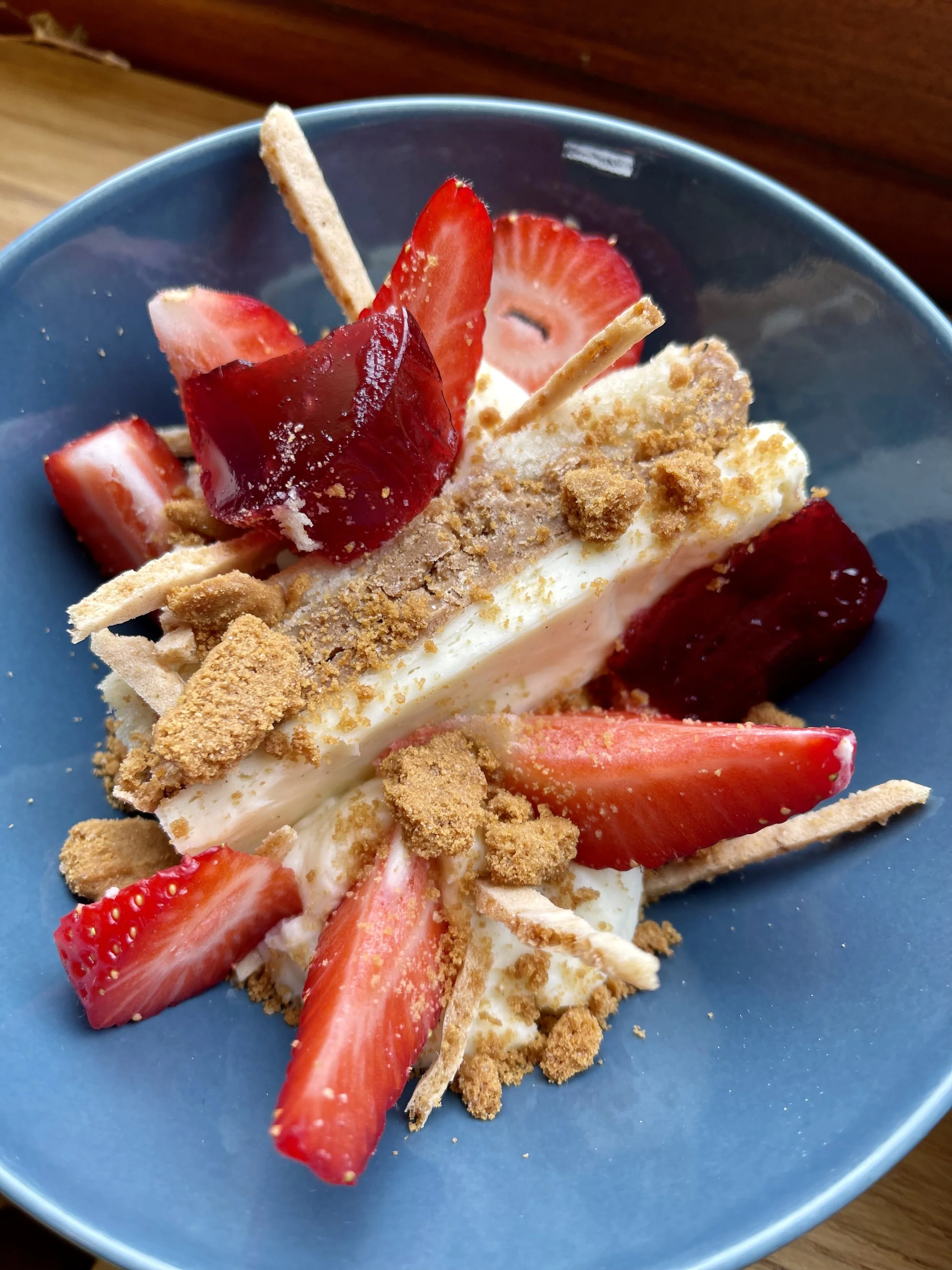Dessert avec fraises coupées, biscuits, crème ou fromage blanc, et miettes de biscuits dans un bol vert.