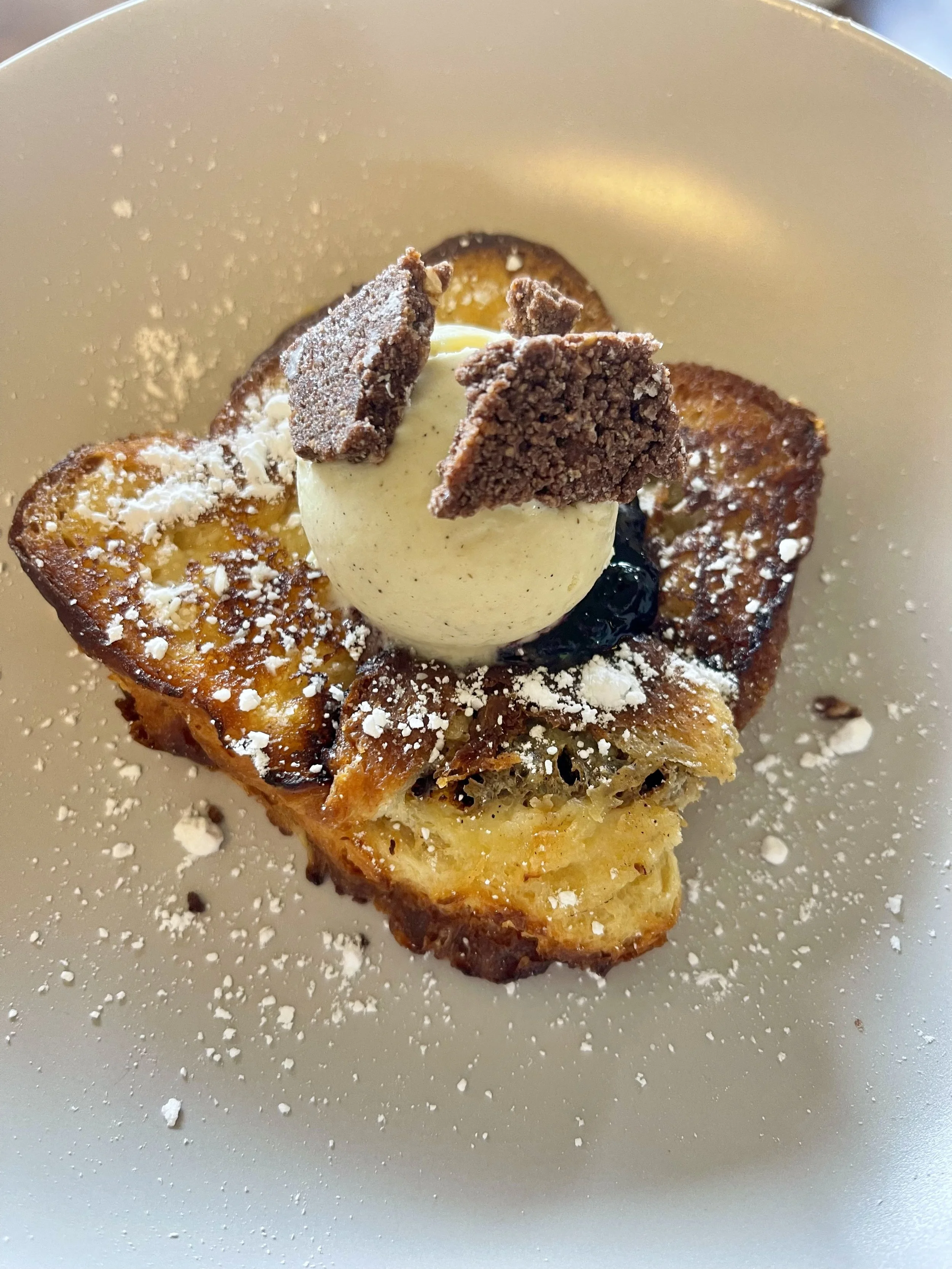 Dessert avec une tranche de gâteau croustillant, une boule de glace ou sorbet, des morceaux de biscuits ou chocolat, et saupoudré de poudre blanche, presentation élégante.