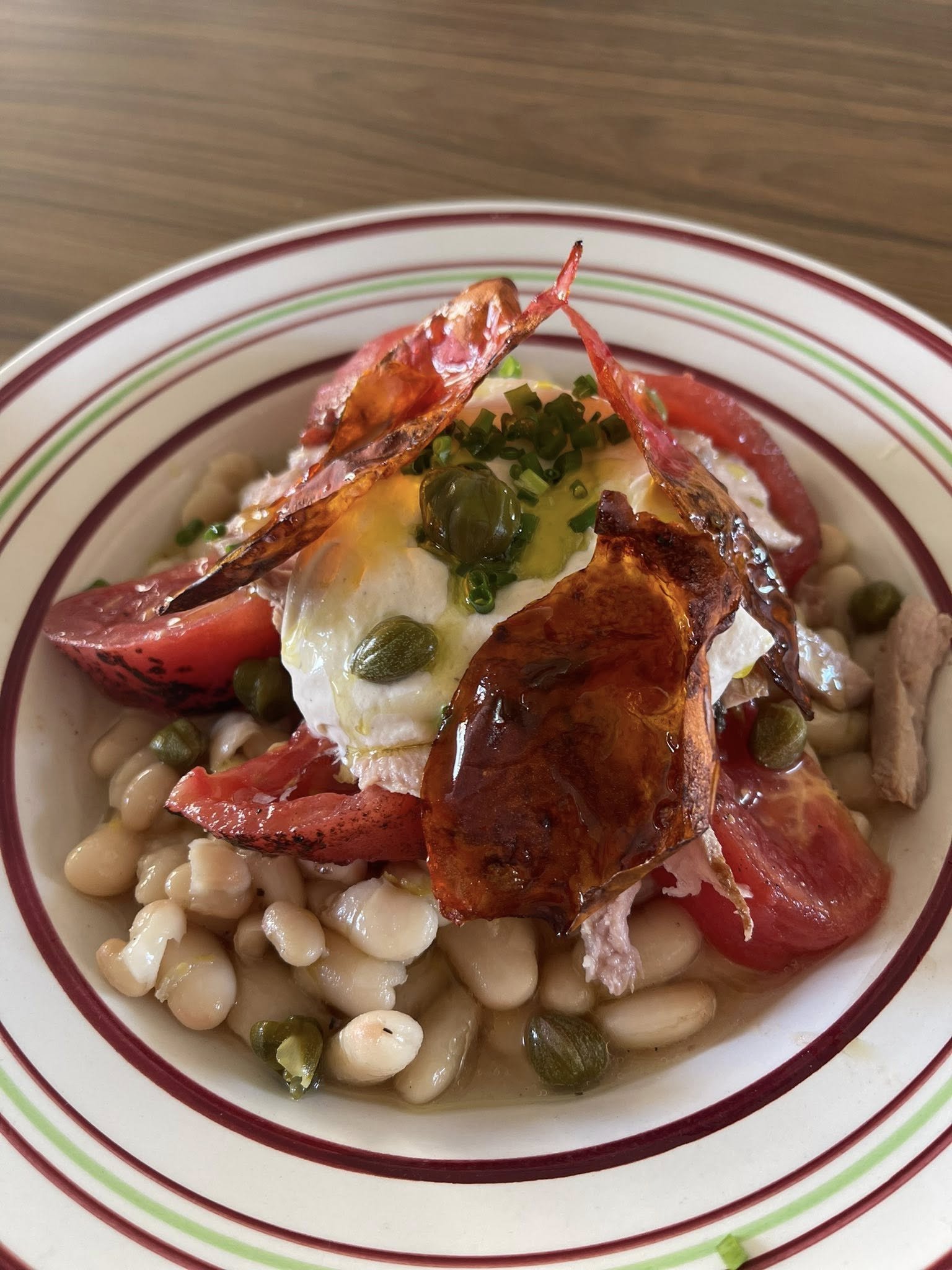 Salade de haricots blancs avec tomate, œuf poché, bacon croustillant, capres, et herbes, dans une assiette