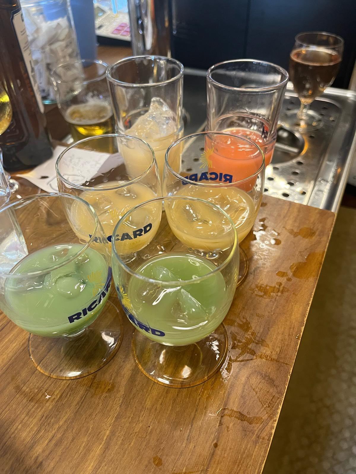 Verres avec différentes boissons colorées sur un comptoir en bois, avec des glaçons et des boissons gazeuses.
