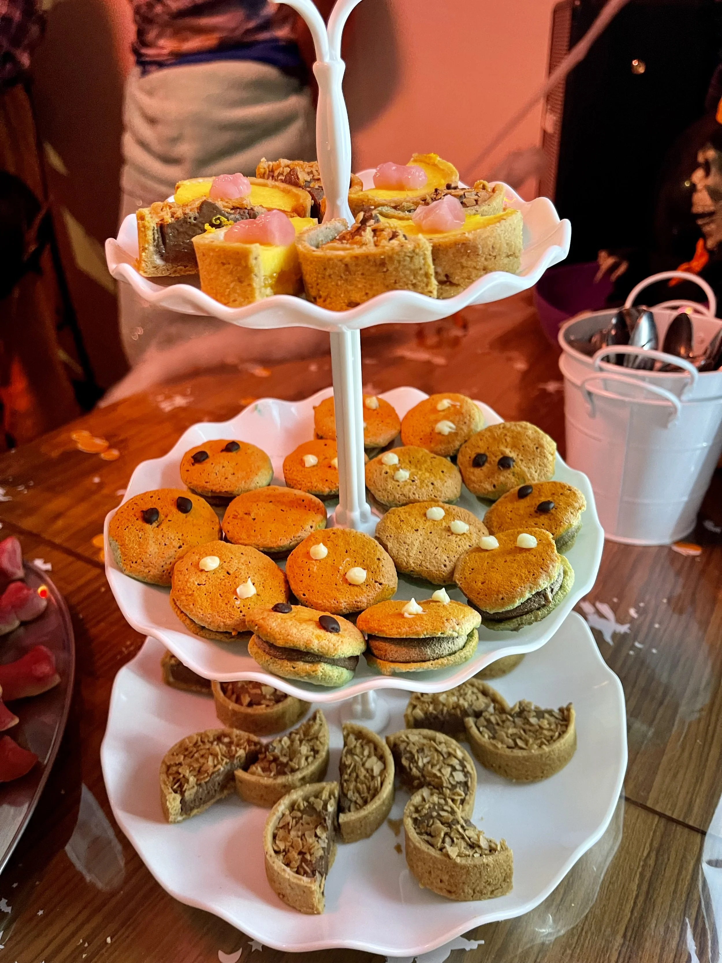 Un trois étages de desserts avec des biscuits aux amandes, des petits gâteaux à la noix de pécan et des entremets au chocolat, présenté sur un support en porcelaine blanc.