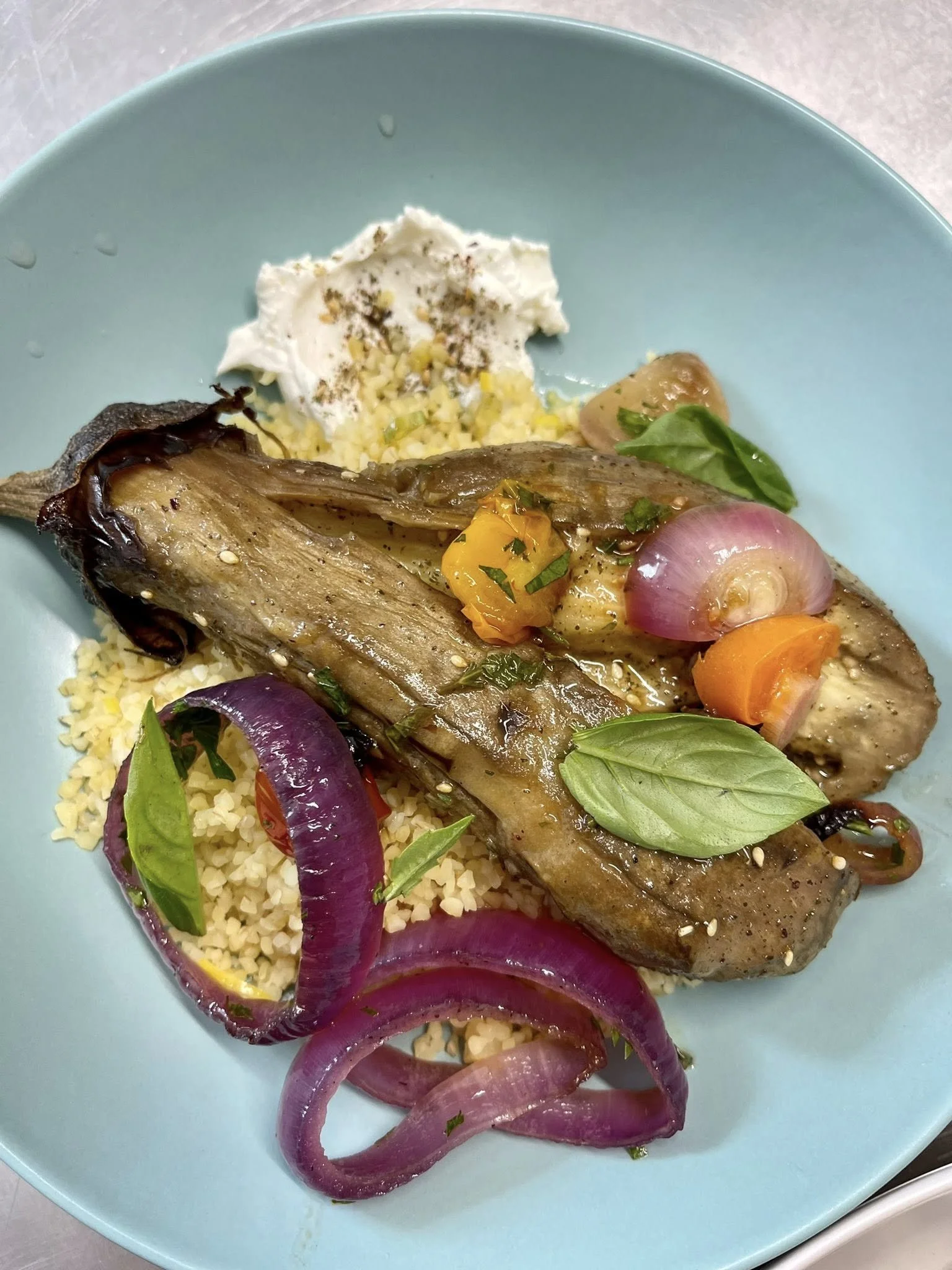 Poisson grillé avec légumes, couscous, et sauce blanche, garnis de basilic.