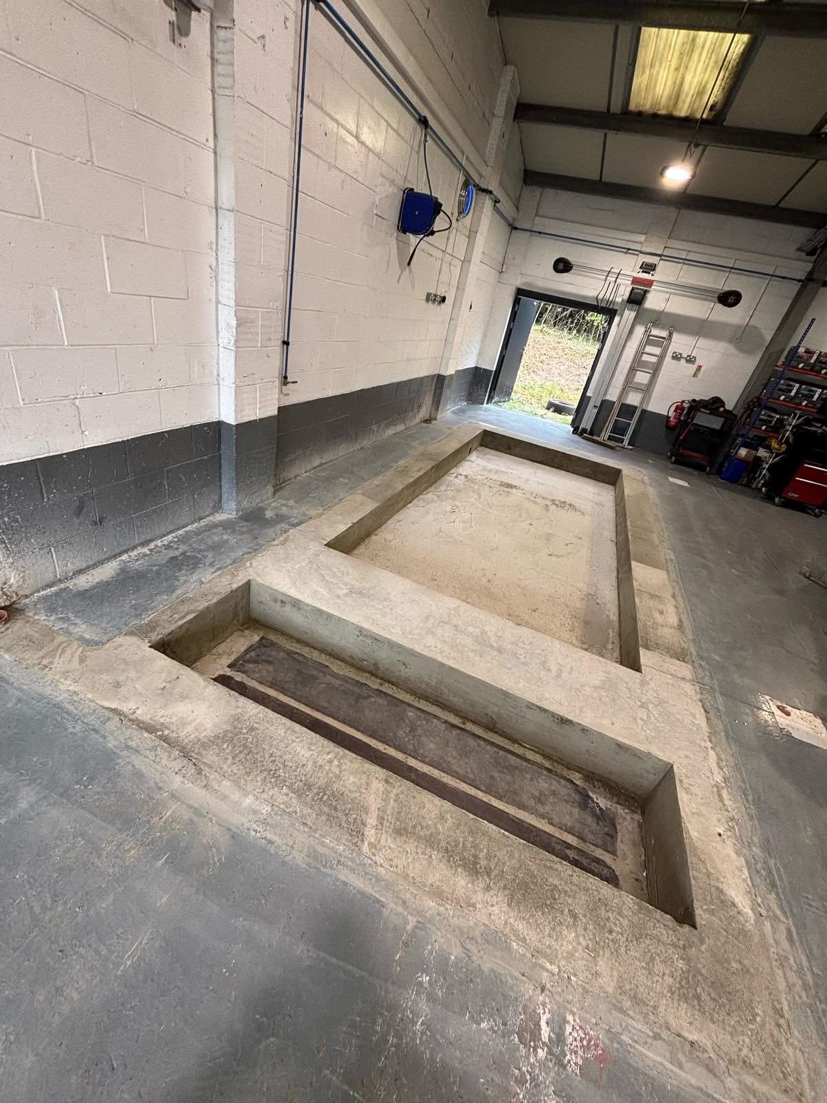 Concrete structural foundation in a garage or workshop with a large rectangular pit and a smaller adjacent rectangular section.