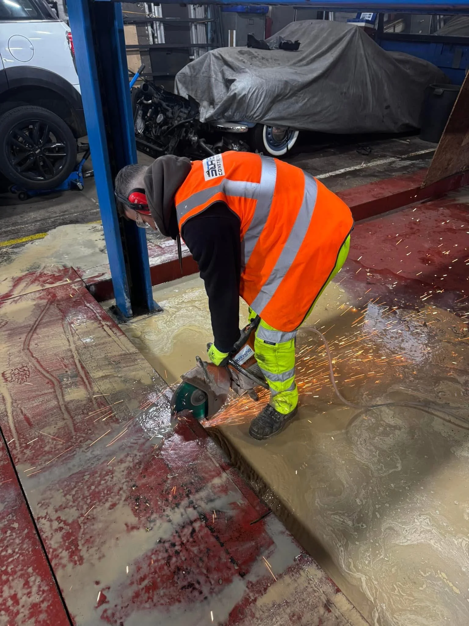 Worker using a power saw to cut concrete while sparks fly in an industrial setting.