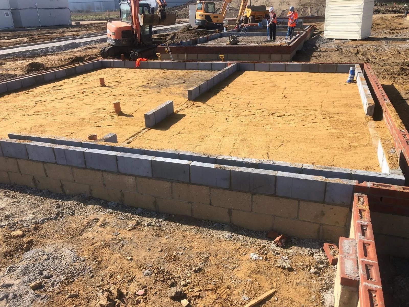 Construction site with foundation being built, showing concrete blocks, workers, and construction equipment.