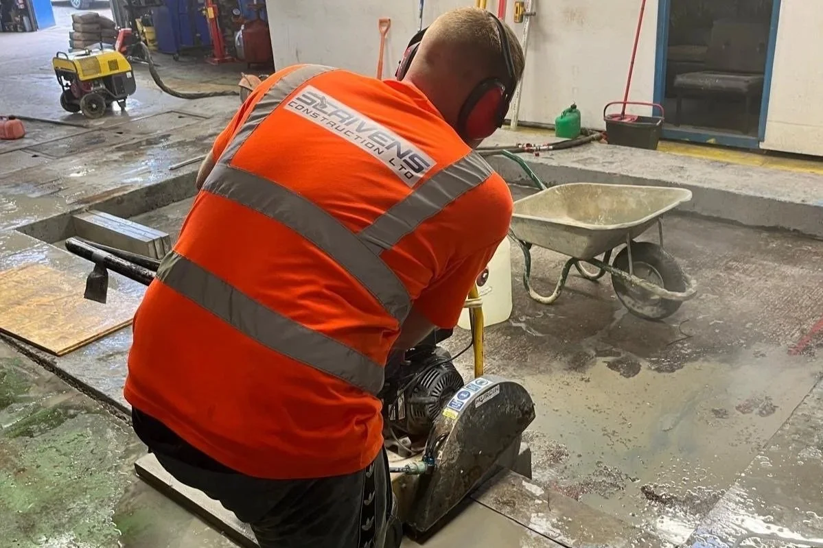 Construction worker operating a concrete saw on a wet floor in a construction site.