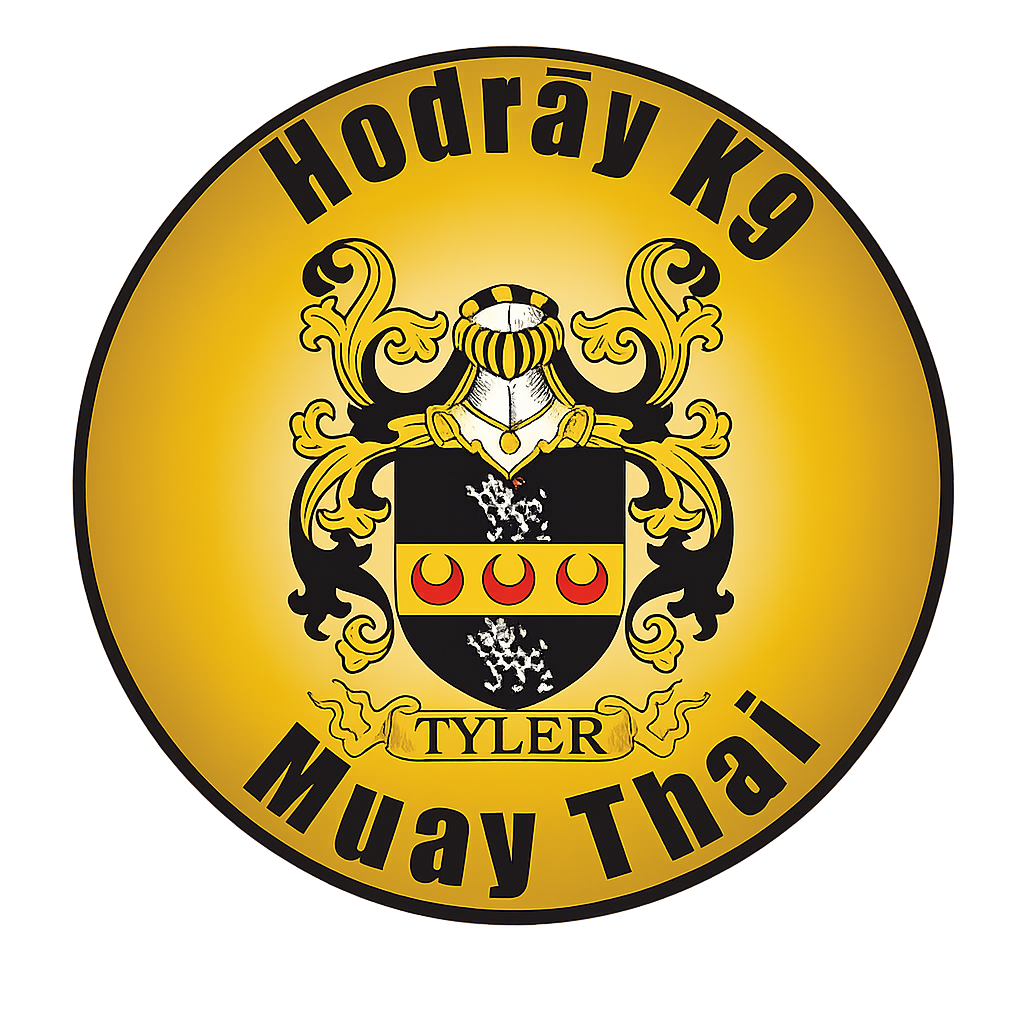 A circular emblem with a gold background and black text that reads 'Hodrāy K9 Muay Thai'. The emblem features a shield with a black top and bottom and gold middle, decorated with three red crescent moons and metallic silver elements. There is ornate gold heraldic decoration around the shield, a knight's helmet, and a banner with the name 'Tyler' at the bottom.