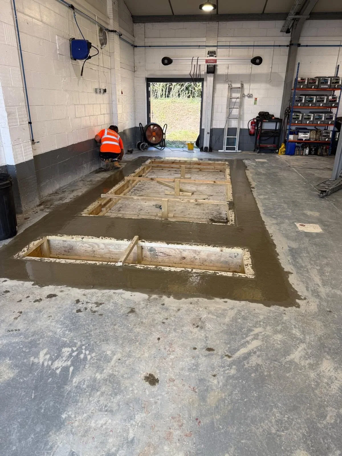 Construction worker in a garage working on concrete floor, with wooden forms and concrete surrounding the unfinished area.