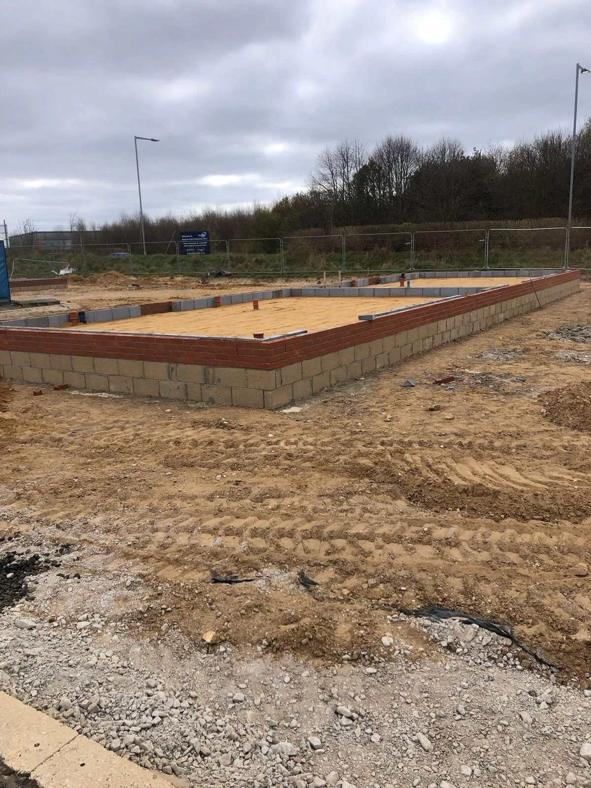 Construction site with a building foundation made of bricks and concrete blocks, surrounded by dirt and gravel, under cloudy skies.