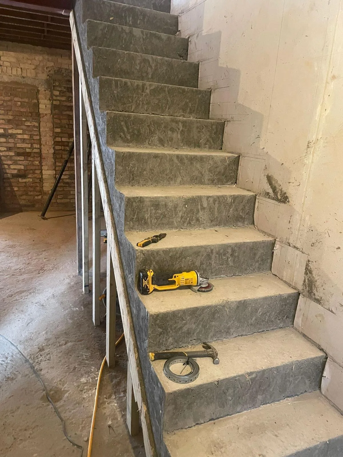 Construction site of a newly installed staircase with concrete steps, tools laid on steps, and unfinished walls.