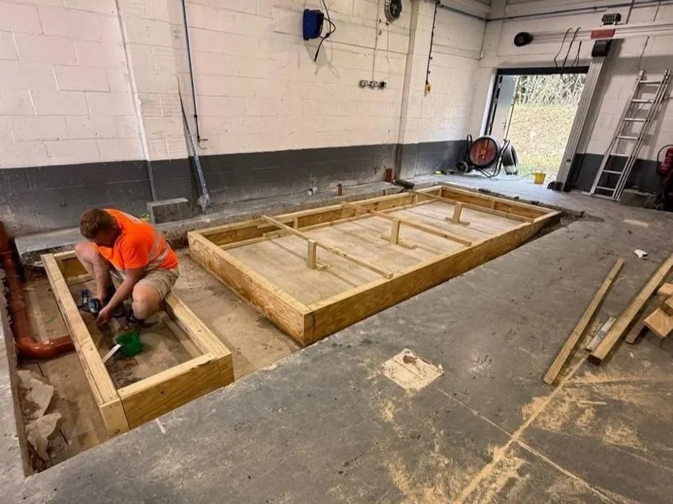 A man working on a construction project inside a garage or workshop, building a wooden frame for a structure with two separate sections.