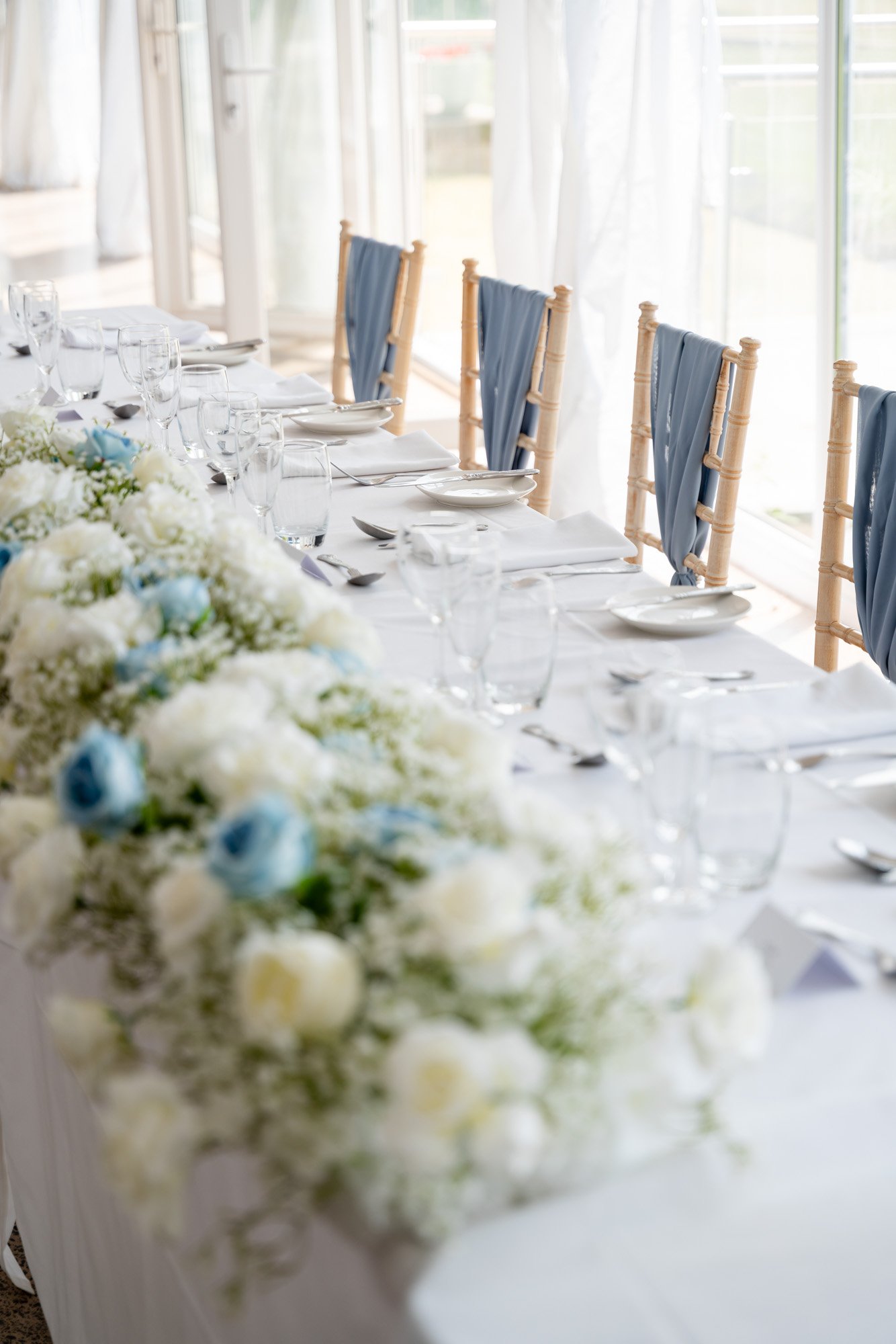 pretty top table during wedding with white and blue rose table runner and blue sashes on chiavari chairs