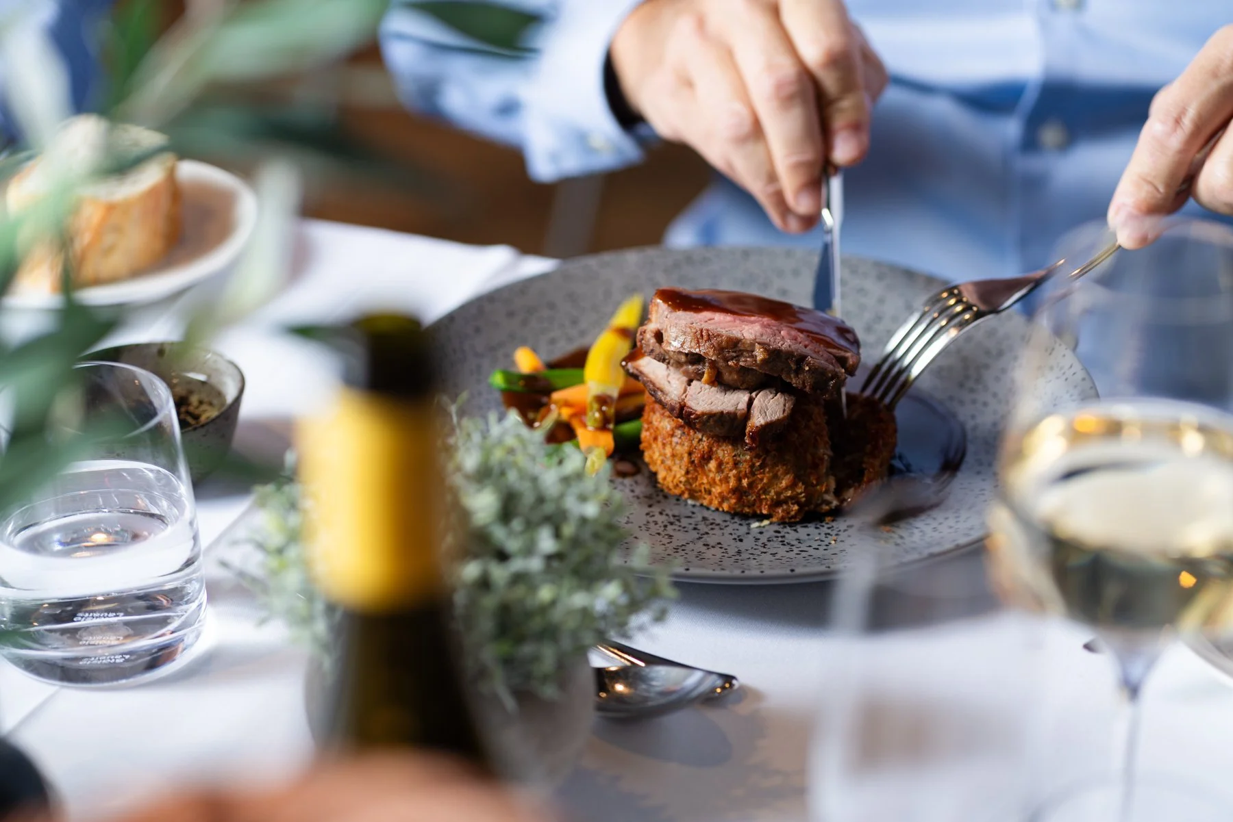 man cutting into meat dish at table