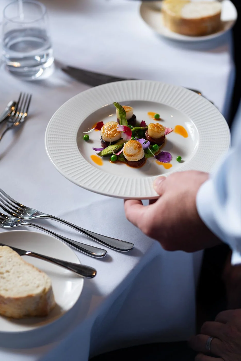 plate of scallops, salad and edible flowers set down on table - spiros caterers