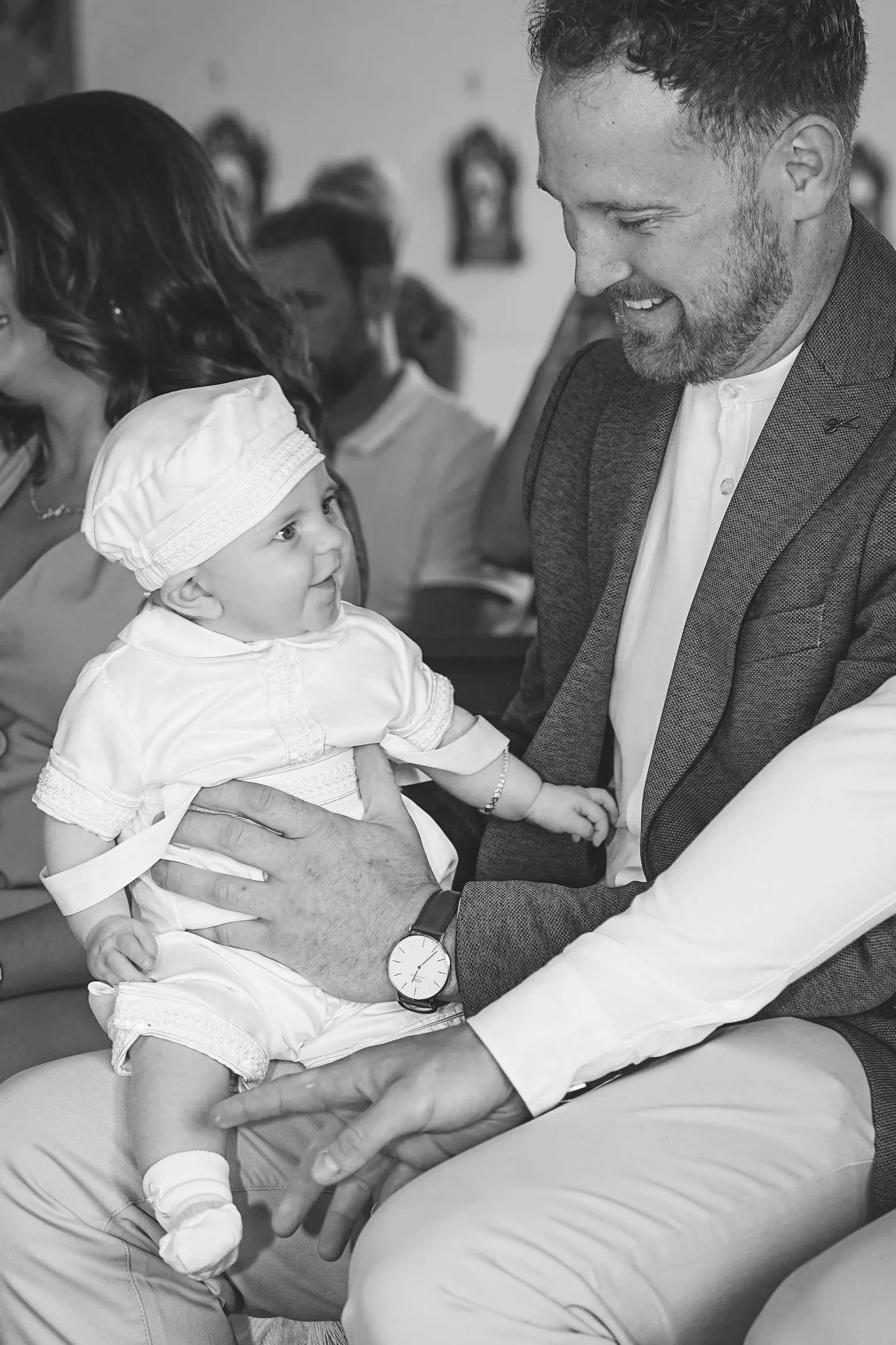 A man holding a baby girl at her christening in Kerry and looking at her with a smile in a gathering setting.