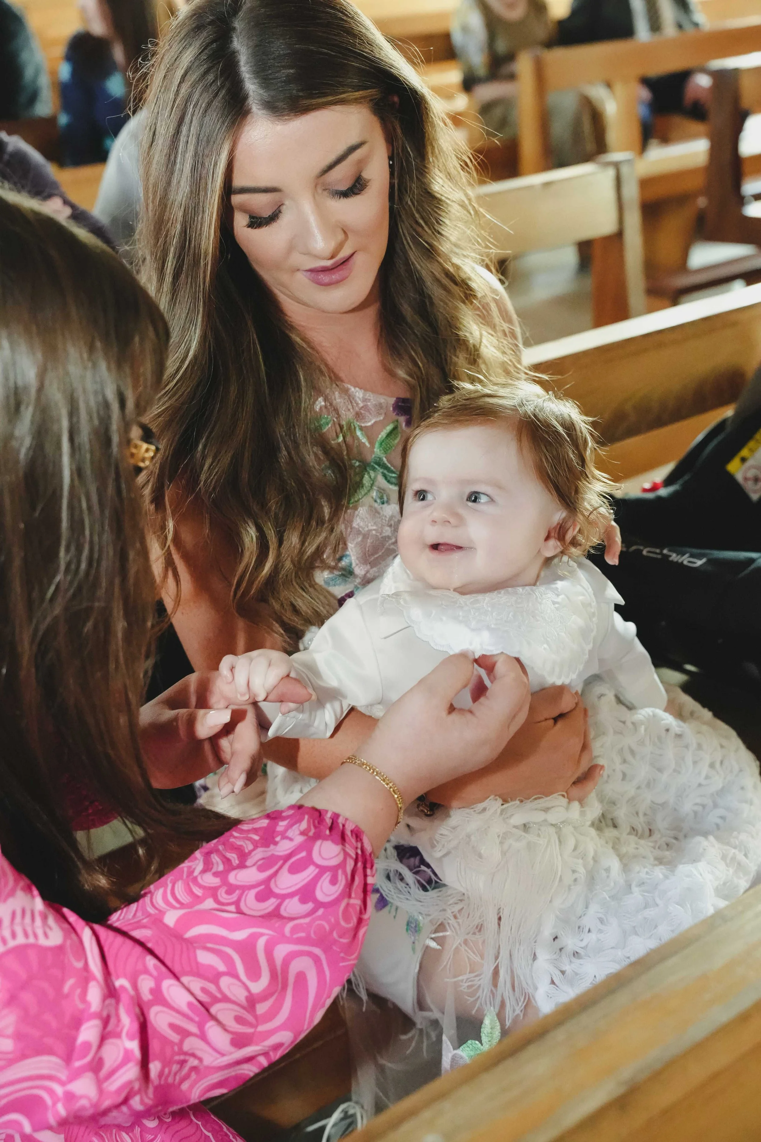 A photograph of a mother holding a smiling baby boy in a church during his christening ceremony in Ballyheigue, Co.Kerry.
