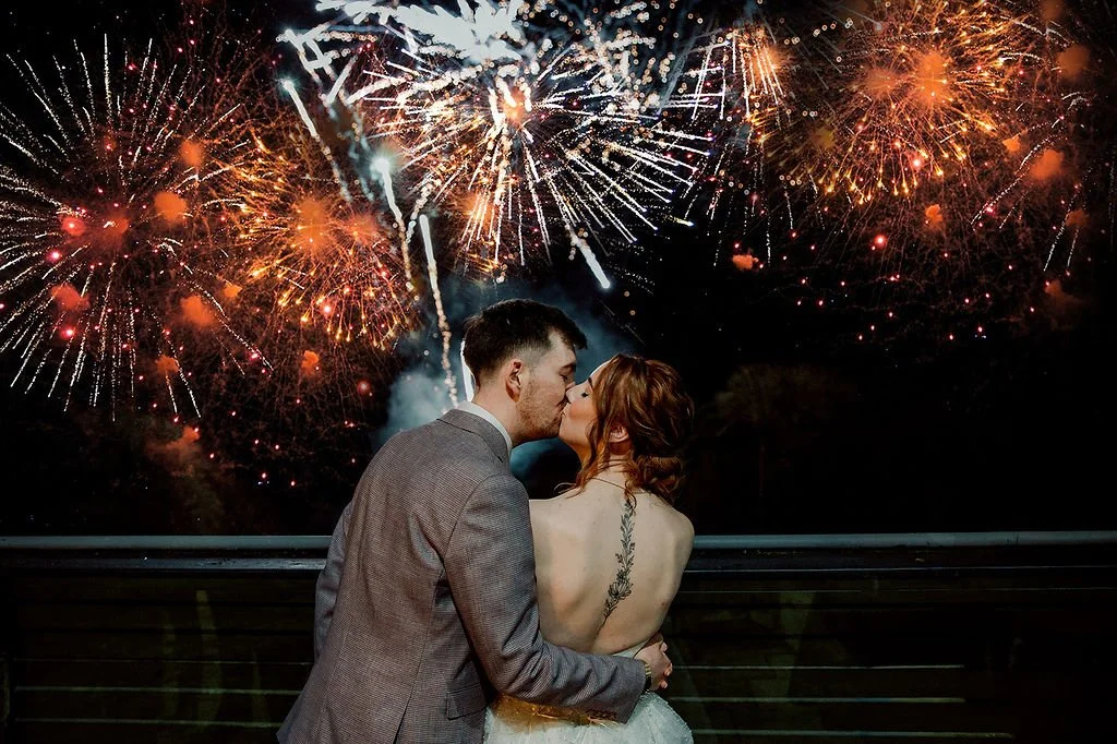 Couple kissing on balcony during fireworks celebration at night.