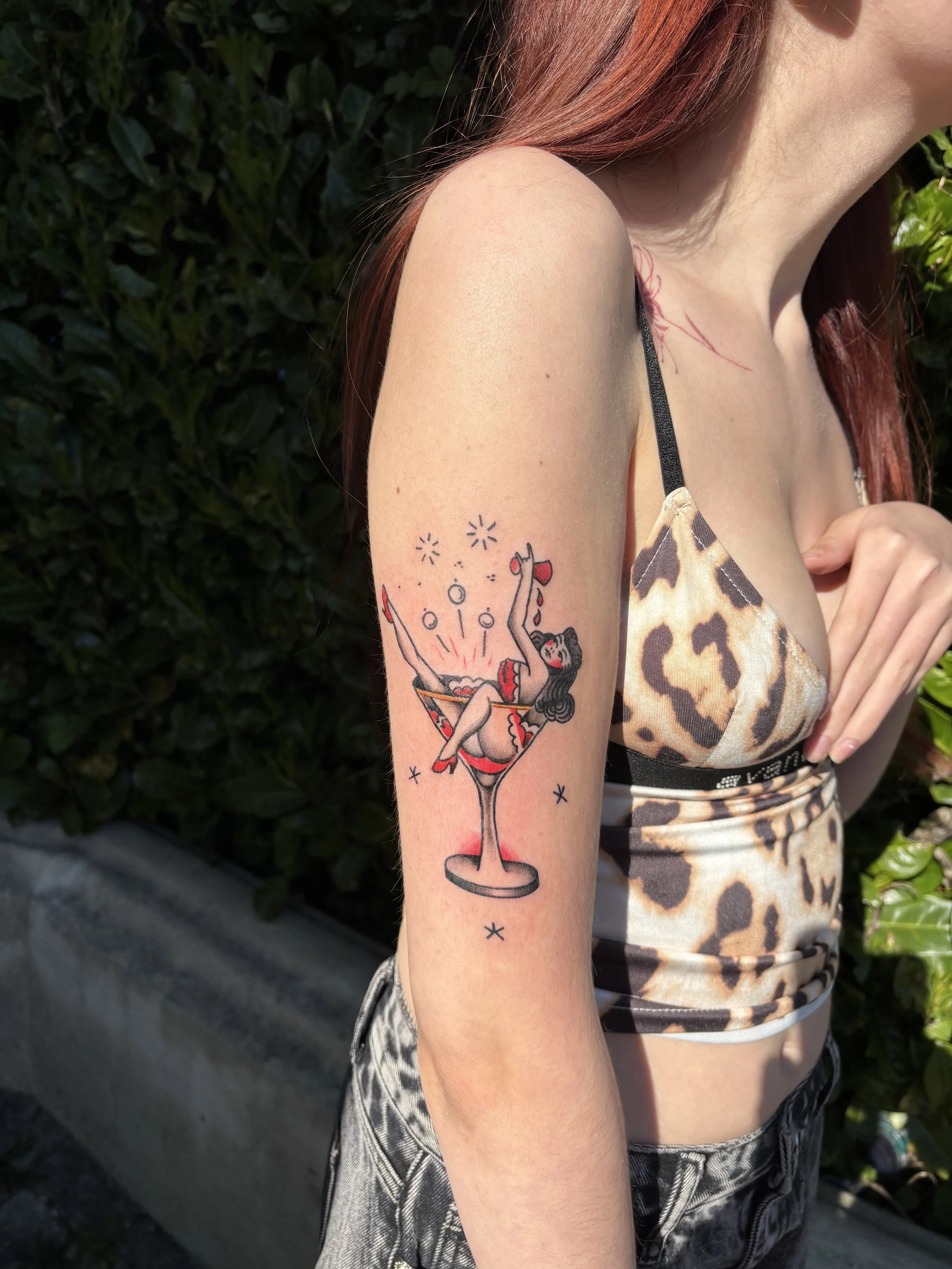 Tattoo of a woman in a red dress sitting inside a cocktail glass on a woman's upper arm.