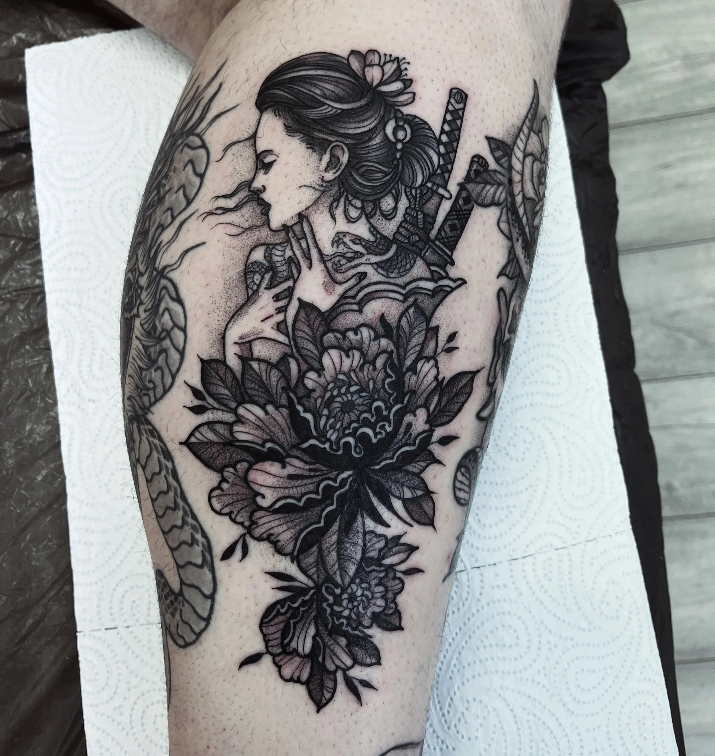 Tattoo of a woman with braided hair and flowers, with swords on her back and large floral design on her chest.