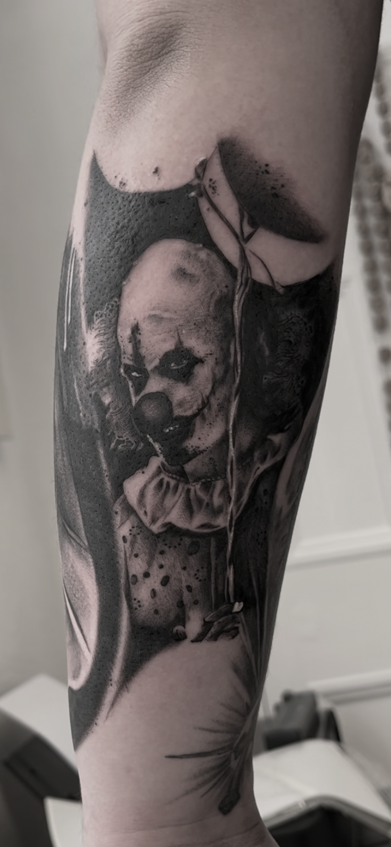 Black and gray tattoo of a clown with makeup, wearing a ruffled collar, holding a balloon, with dramatic shading and details.