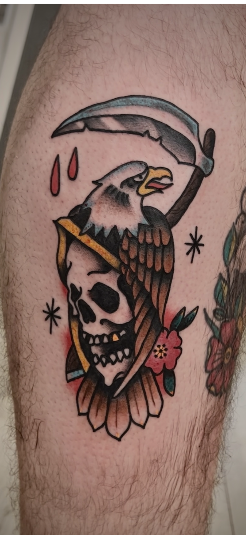 Tattoo of an eagle with a skull, holding a sickle under a scythe, surrounded by flowers and stars.